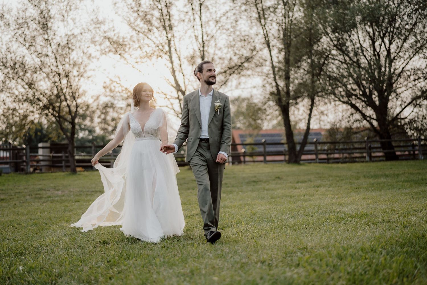 Brautpaar spaziert im Abendlicht auf einer Wiese Hand in Hand, Hochzeit Feldbach