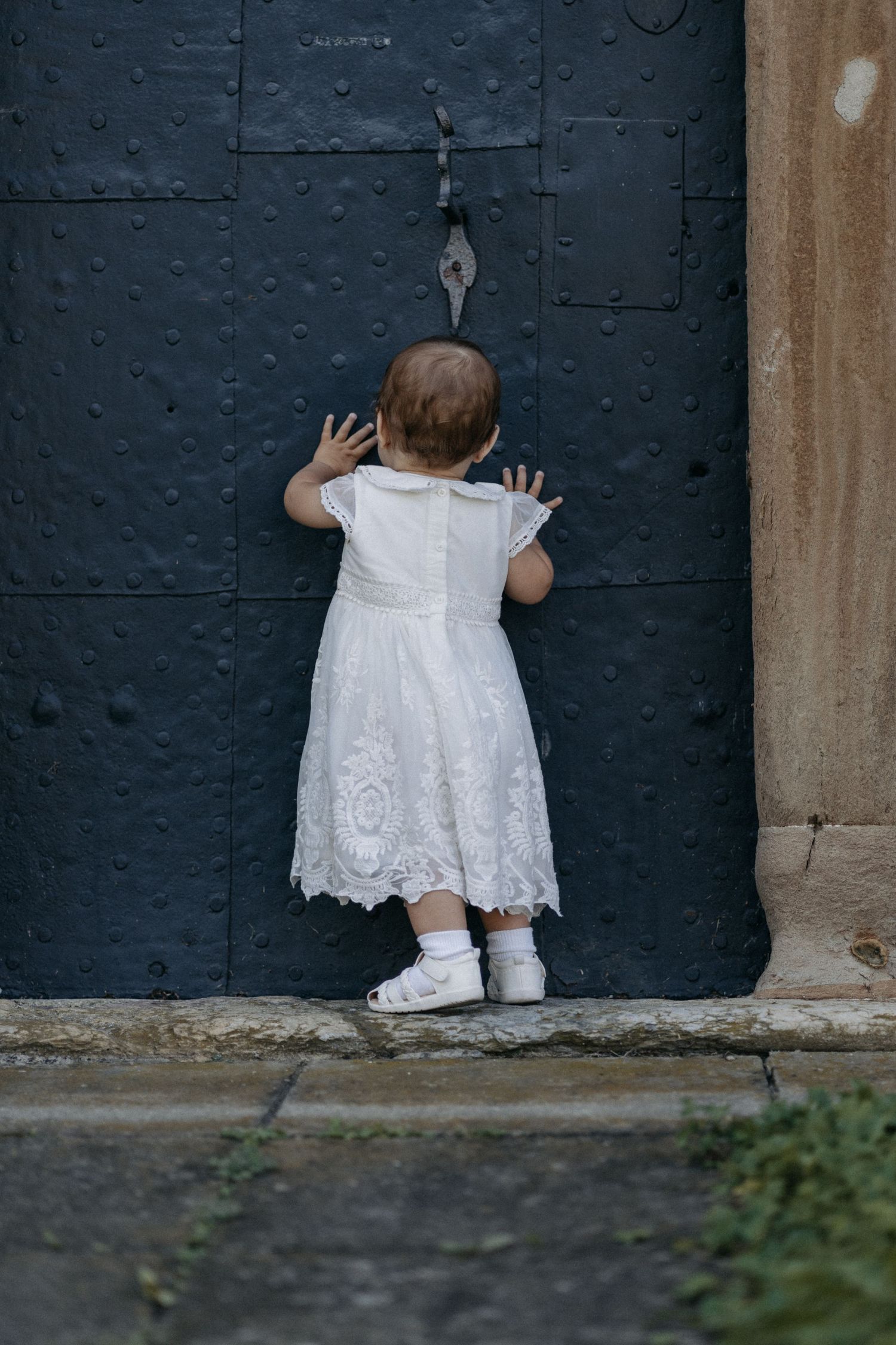 Taufkind vor der Kirche, weißes Kleid, emotionale Fotografie der Taufe