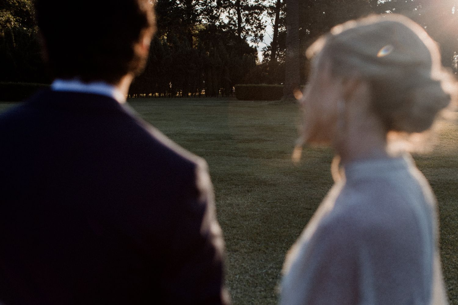 A bride and groom share a romantic golden hour moment outdoors on a lush green lawn at their wedding.