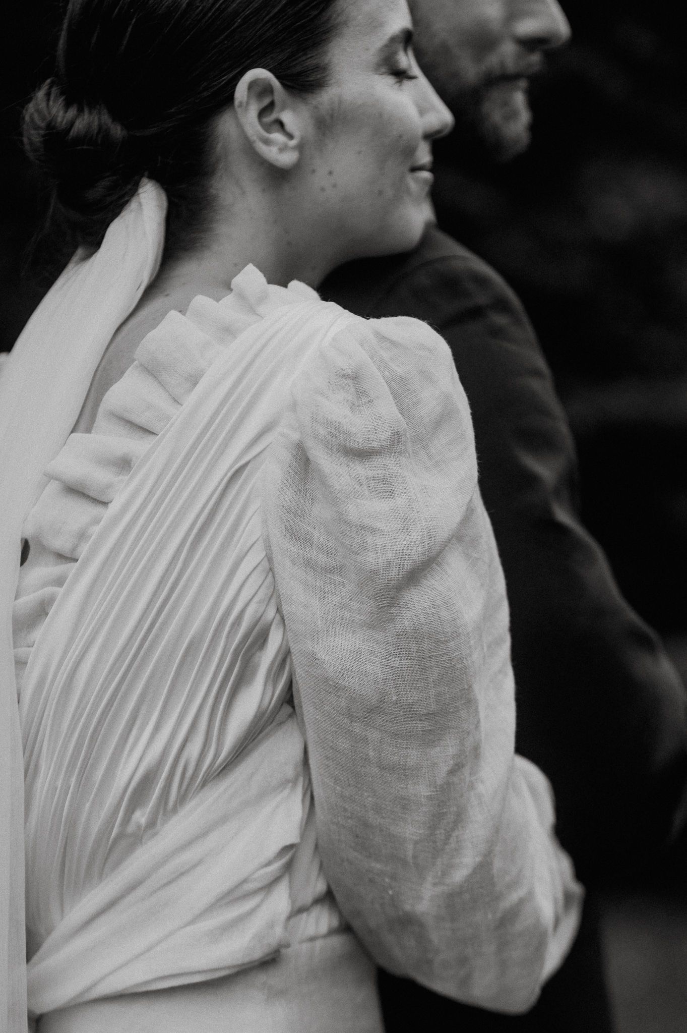 Black and white portrait showing back of vintage-style wedding dress with pleated details and puffy sleeves.