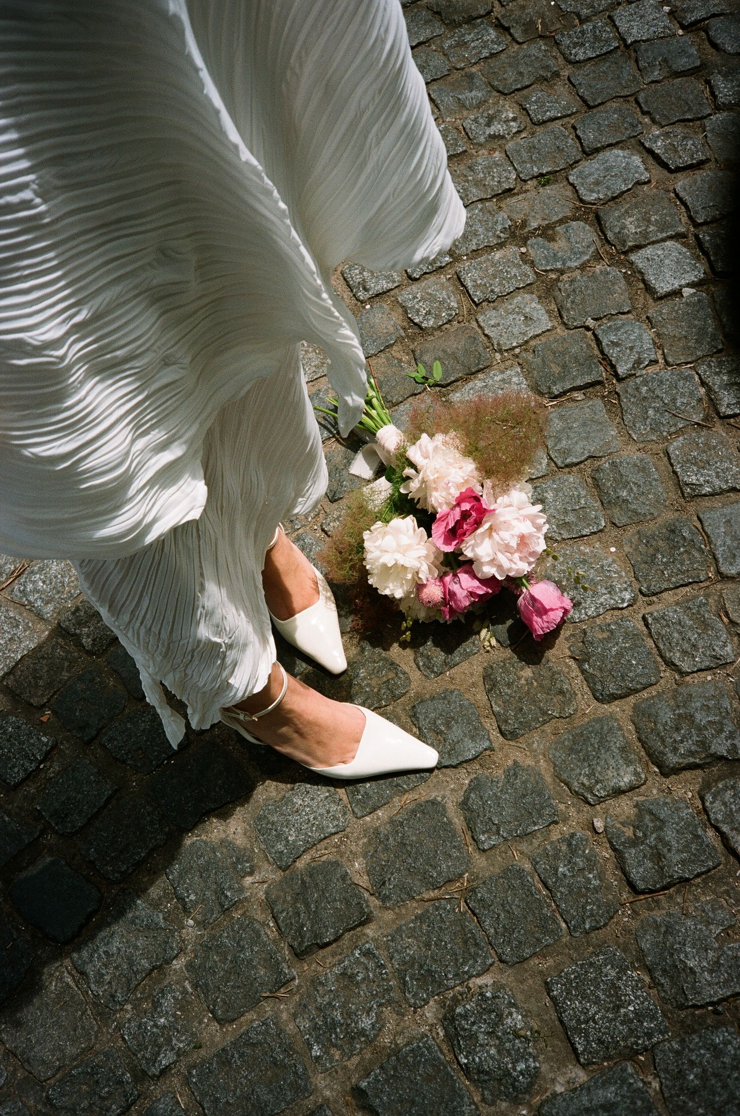 A sequence of images showing white dress hem and shoes walking on cobblestone pavement with scattered flower petals.
