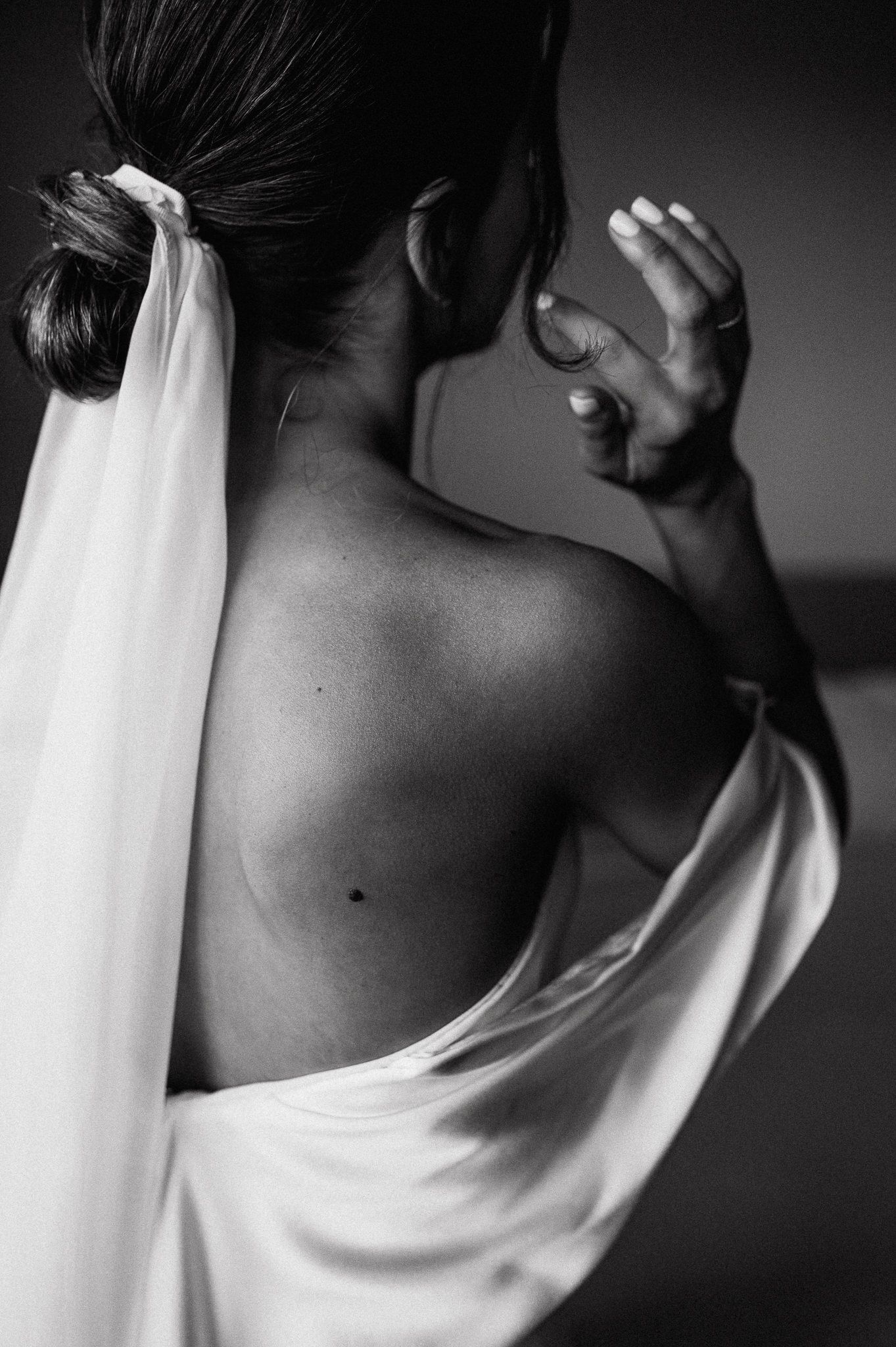 Artistic black and white photograph showing a bare back draped in flowing white fabric against dark background.