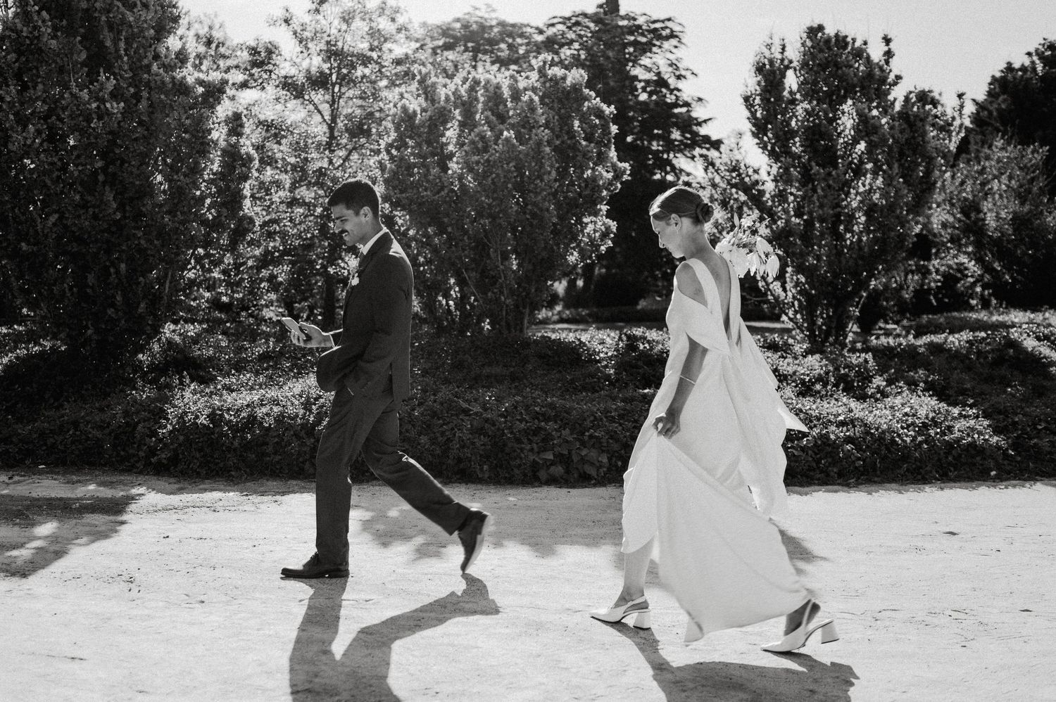 A couple in formal wedding attire poses playfully in a sunlit garden setting during their photo session.