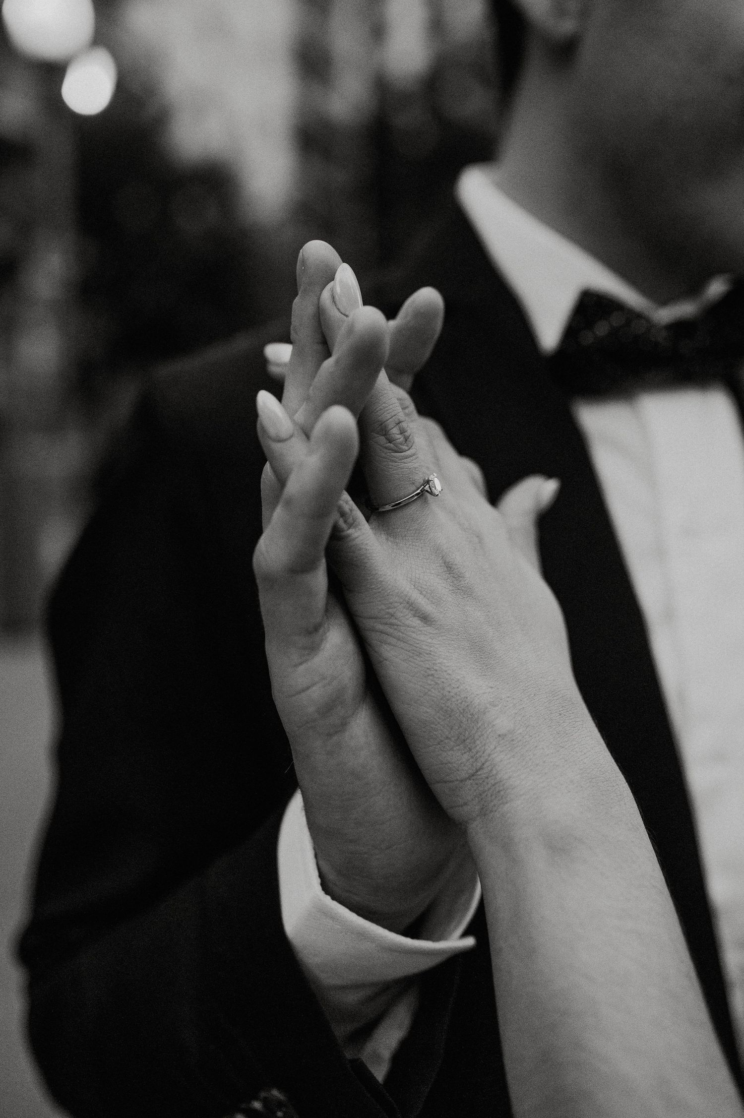 Black and white photo of two hands clasped together in a romantic gesture, with a ring visible on one hand.
