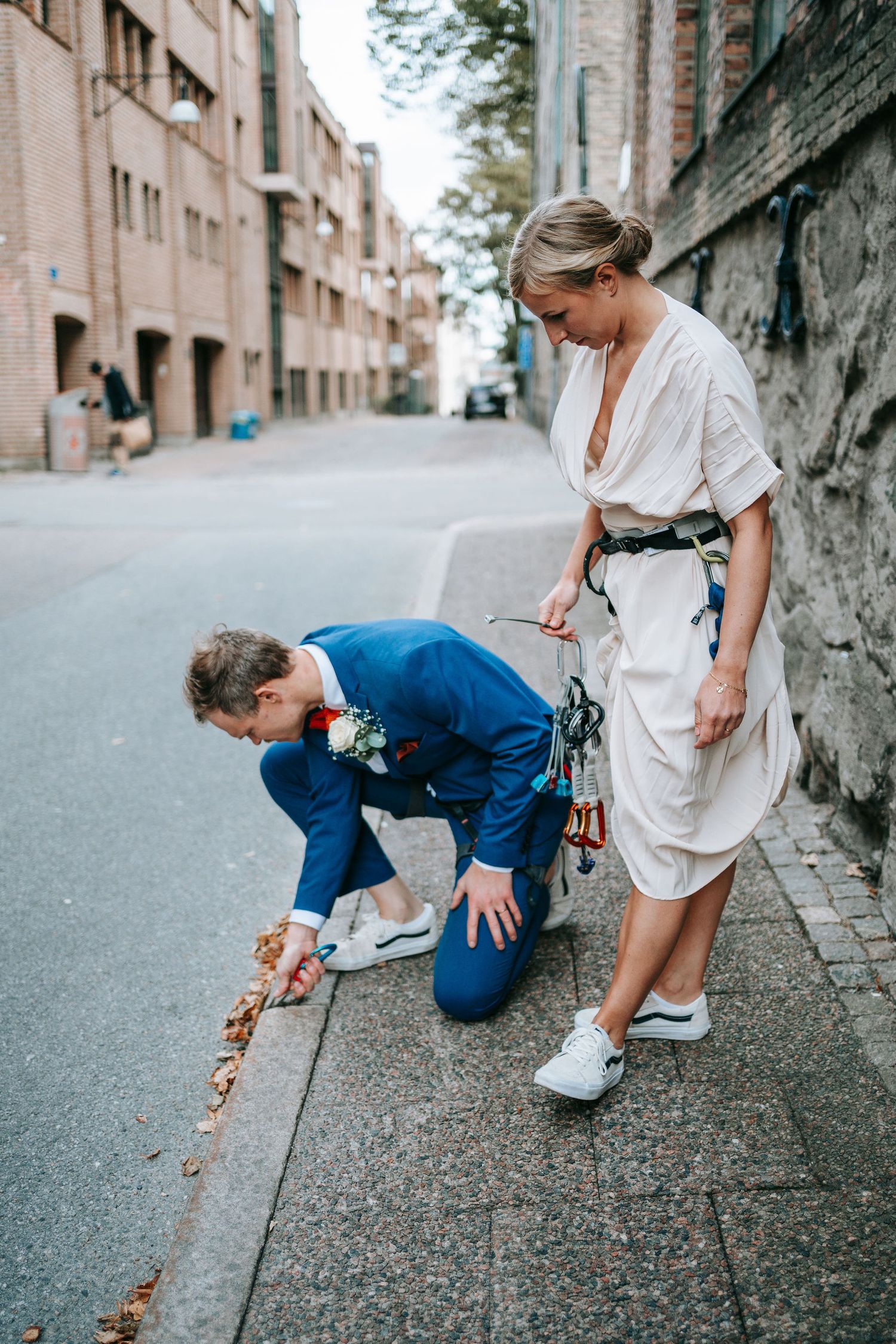 Brudgum förbereder klätterutrustning på gatan medan bruden står bredvid i stadsmiljö i Göteborg, bröllopsfotograf
