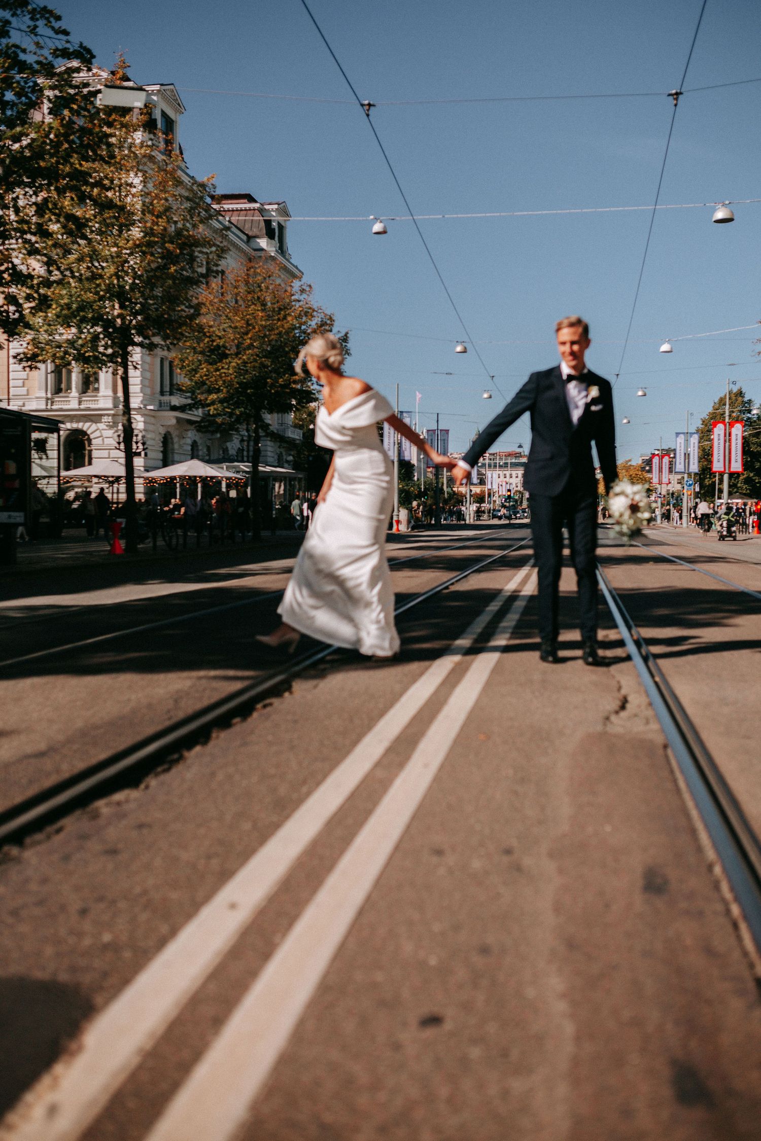 dokumentär bröllopsbild på brudpar som går längst med spårvagnsspåren på avenyn, bröllopsfotografering i centrala göteborg