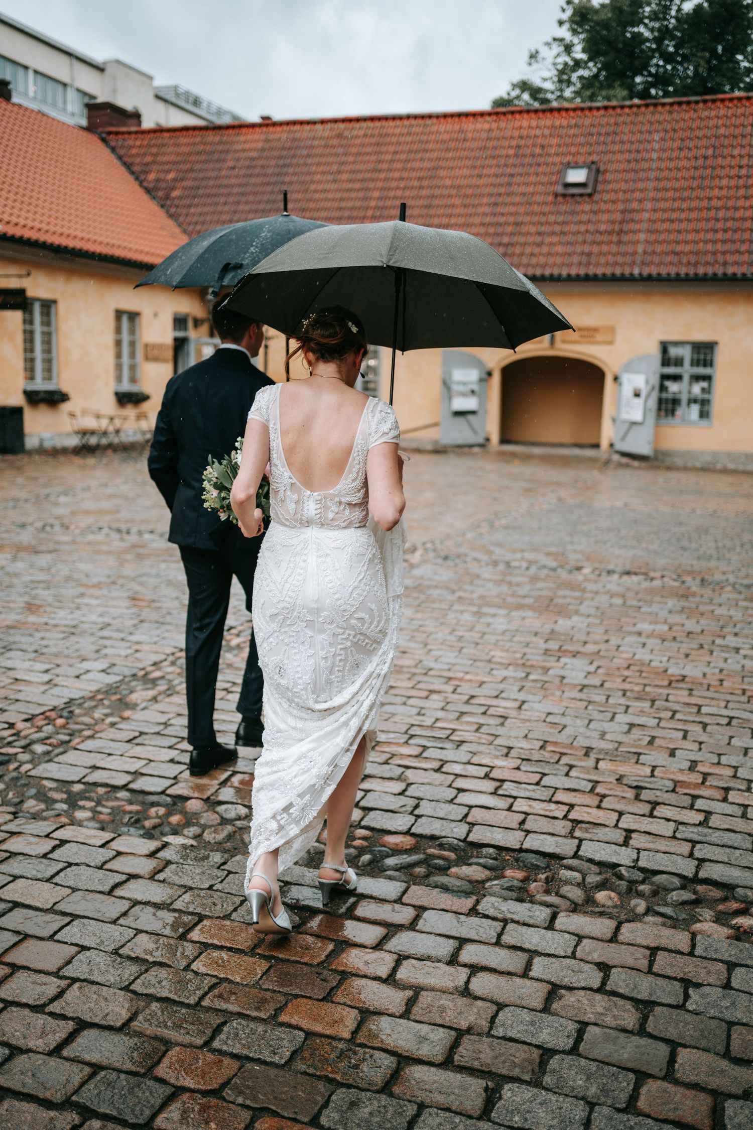 brudpar går i regnet med paraplyn i centrala göteborg på kullerstensgator innan vigsel i rådhuset, bröllopsfotografering kronhusbodarna