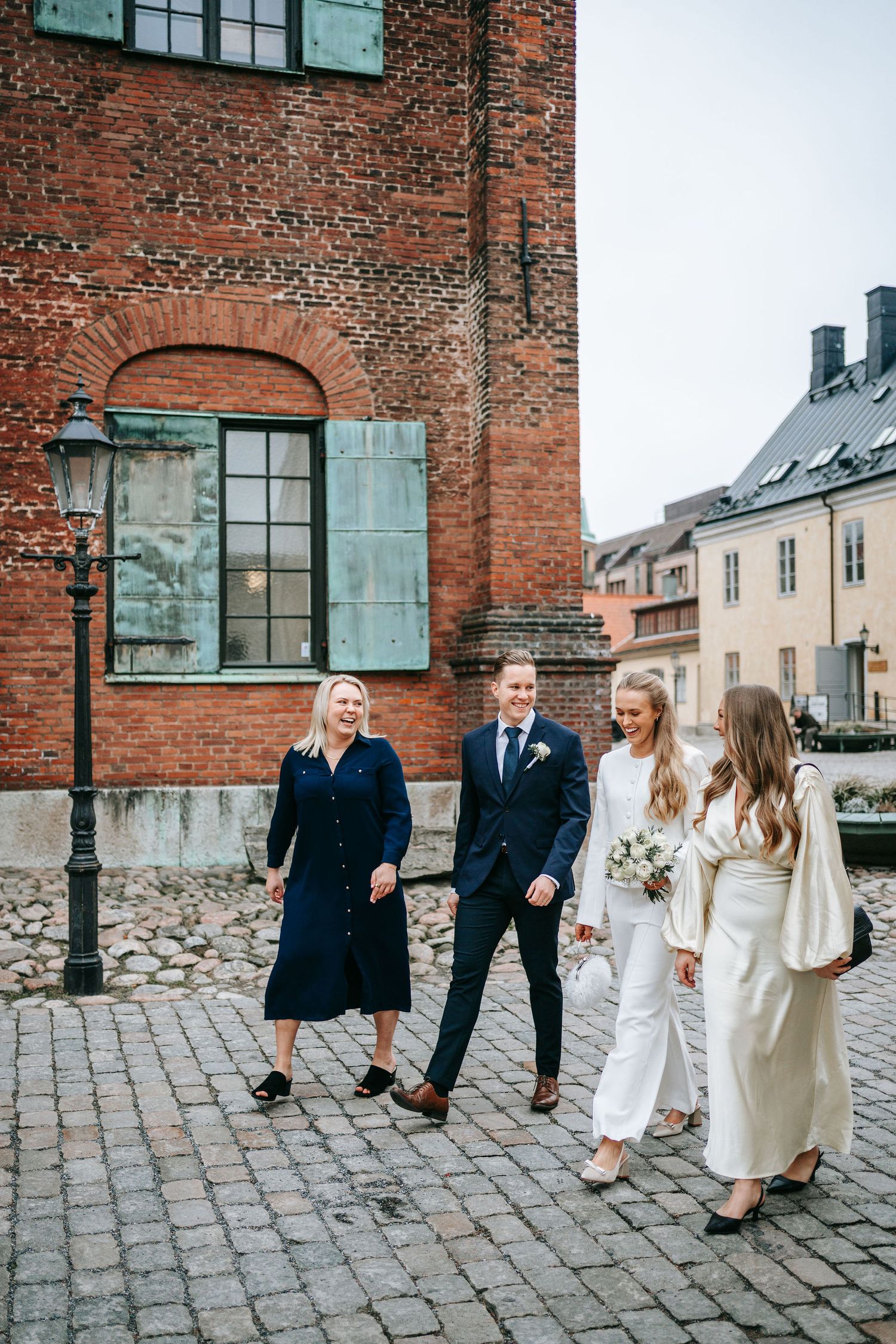Brudpar går på kullerstenarna vid Kronhusbodarna i Göteborg med sina två vittnen