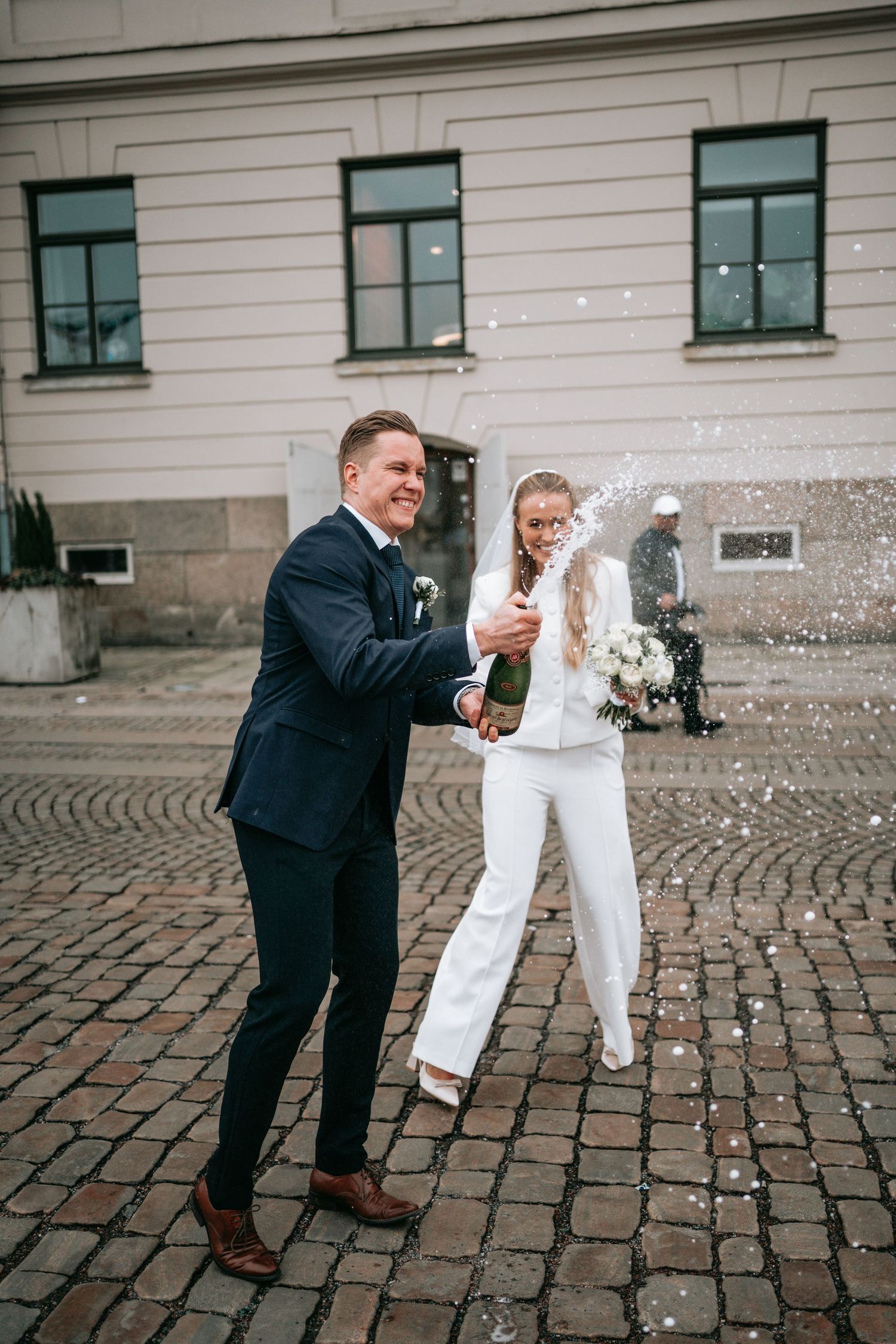 brudgum som poppar en flaska champange utanför rådhuset i göteborg för att fira att de precis gift sig medan bruden står bredvid och skratta