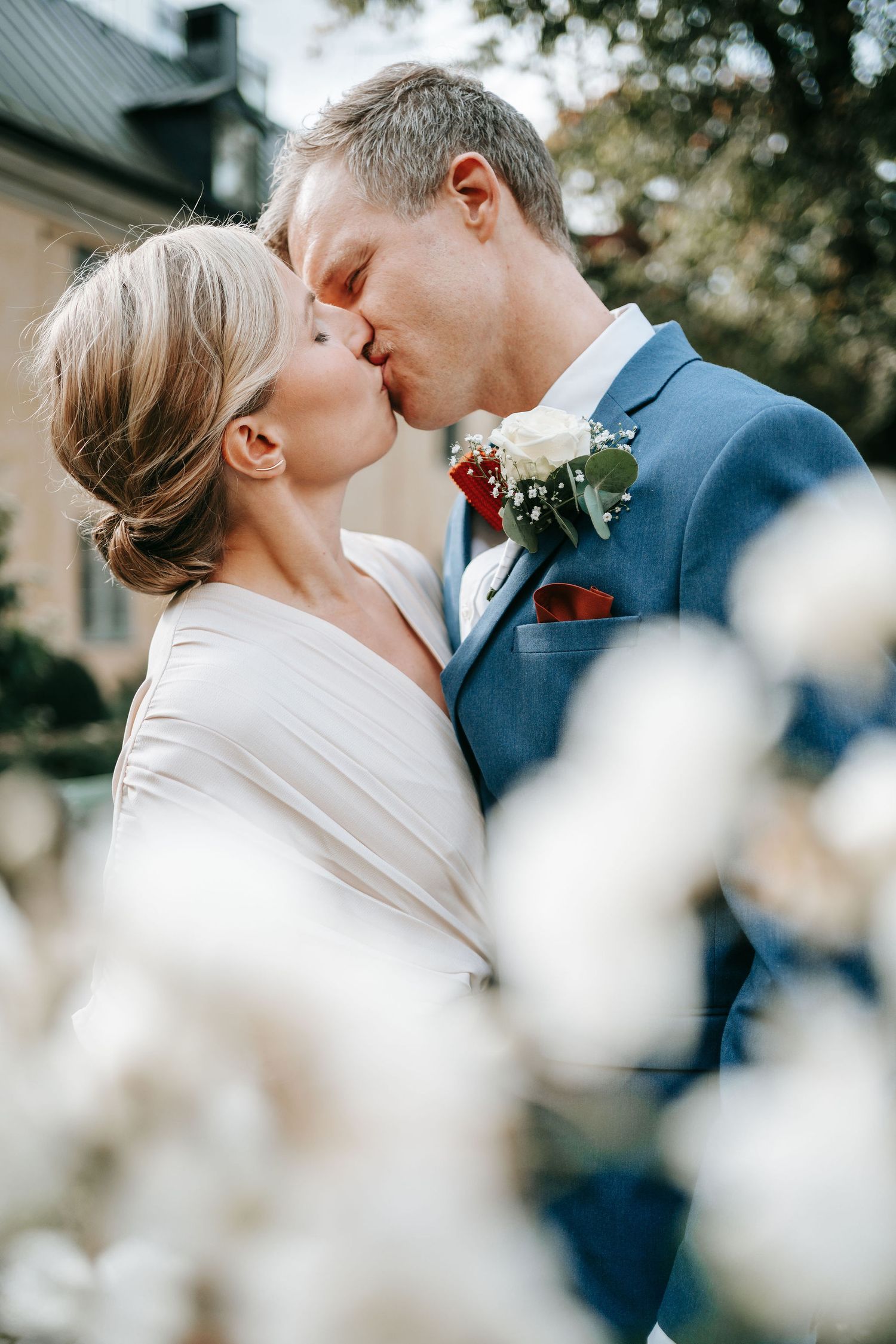 Brud och brudgum kysser varandra i parken vid kronhusbodarna i göteborg innan borglig rådhusvigsel omgivna av vita blommor, bröllopsfotograf