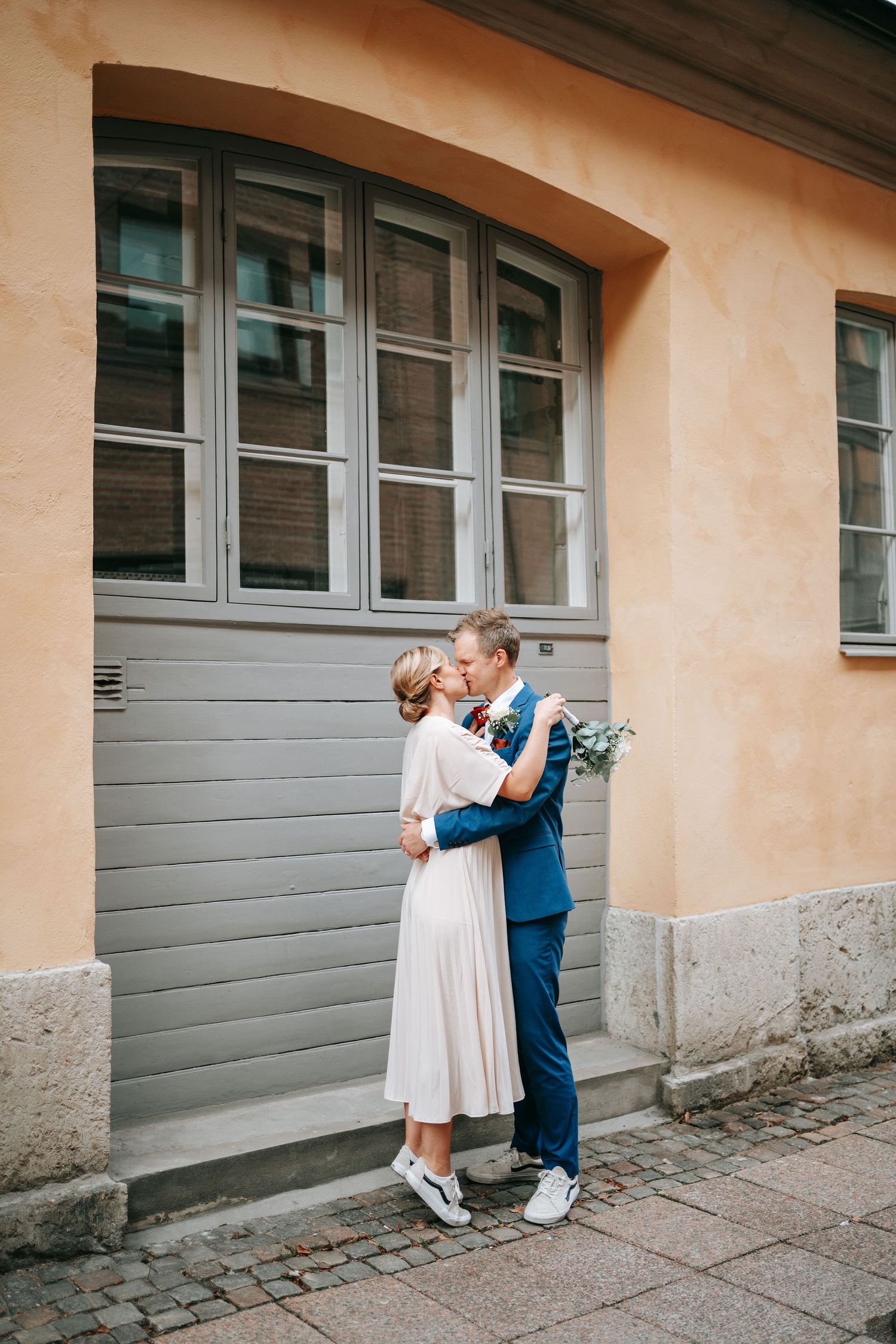 Brudpar delar en kyss framför grå dörr på kullerstensgata i centrala Göteborg nära rådhuset, bröllopsfotografering