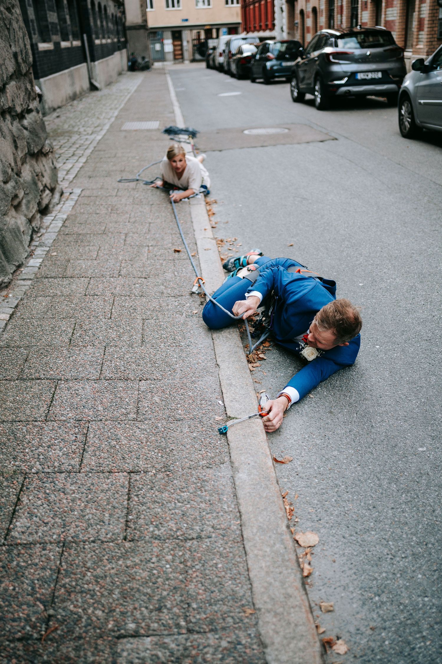 Brud och brudgum ligger tillsammans på gata i Göteborg med klätterrep under lekfull fotografering, unik bröllopsfotografering