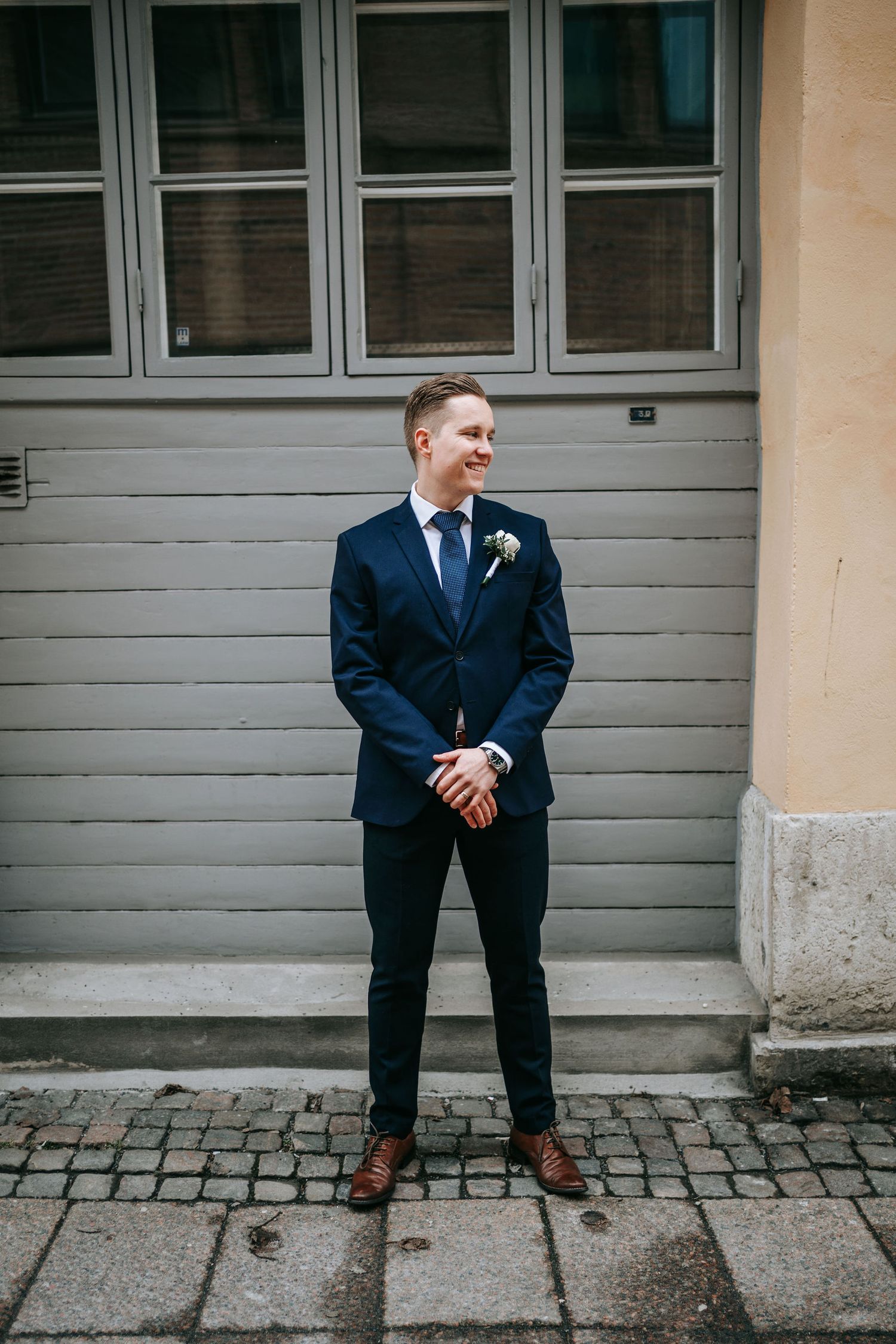Brudgum ler i mörk kostym på kullerstensgata nära rådhuset i Göteborg, fotograf göteborg bröllop