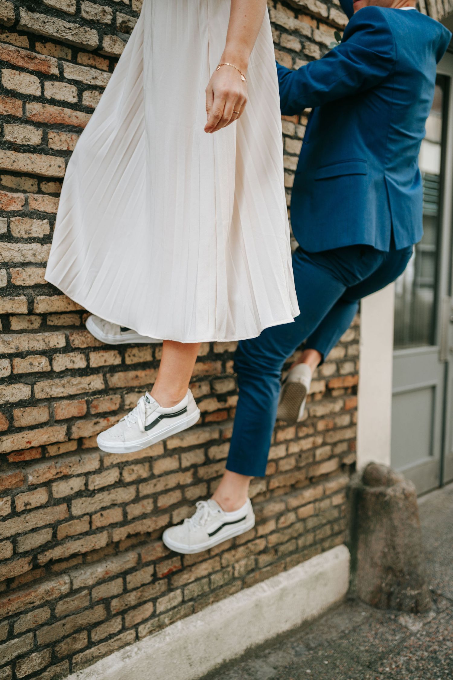 Close-up of couple in wedding attire wearing white sneakers, climbing a brick wall in formal clothes. wedding photographer Gothenburg