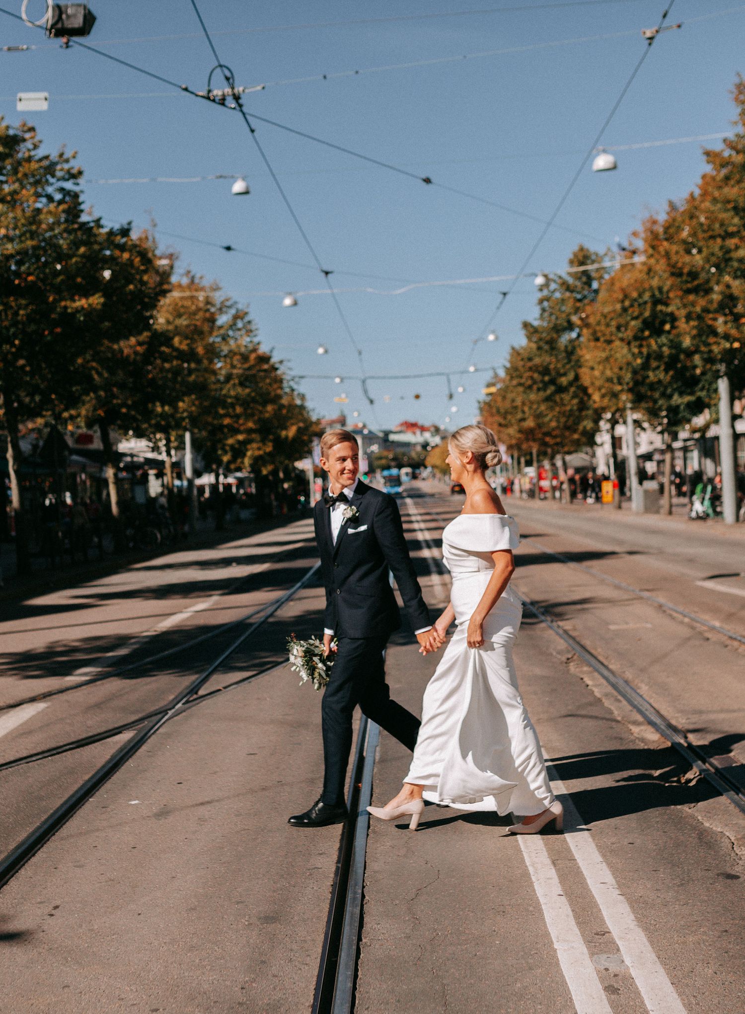 brudpar går över avenyn i göteborg på spårvagnsspåren, bröllopsfotografering i göteborg och på västkusten