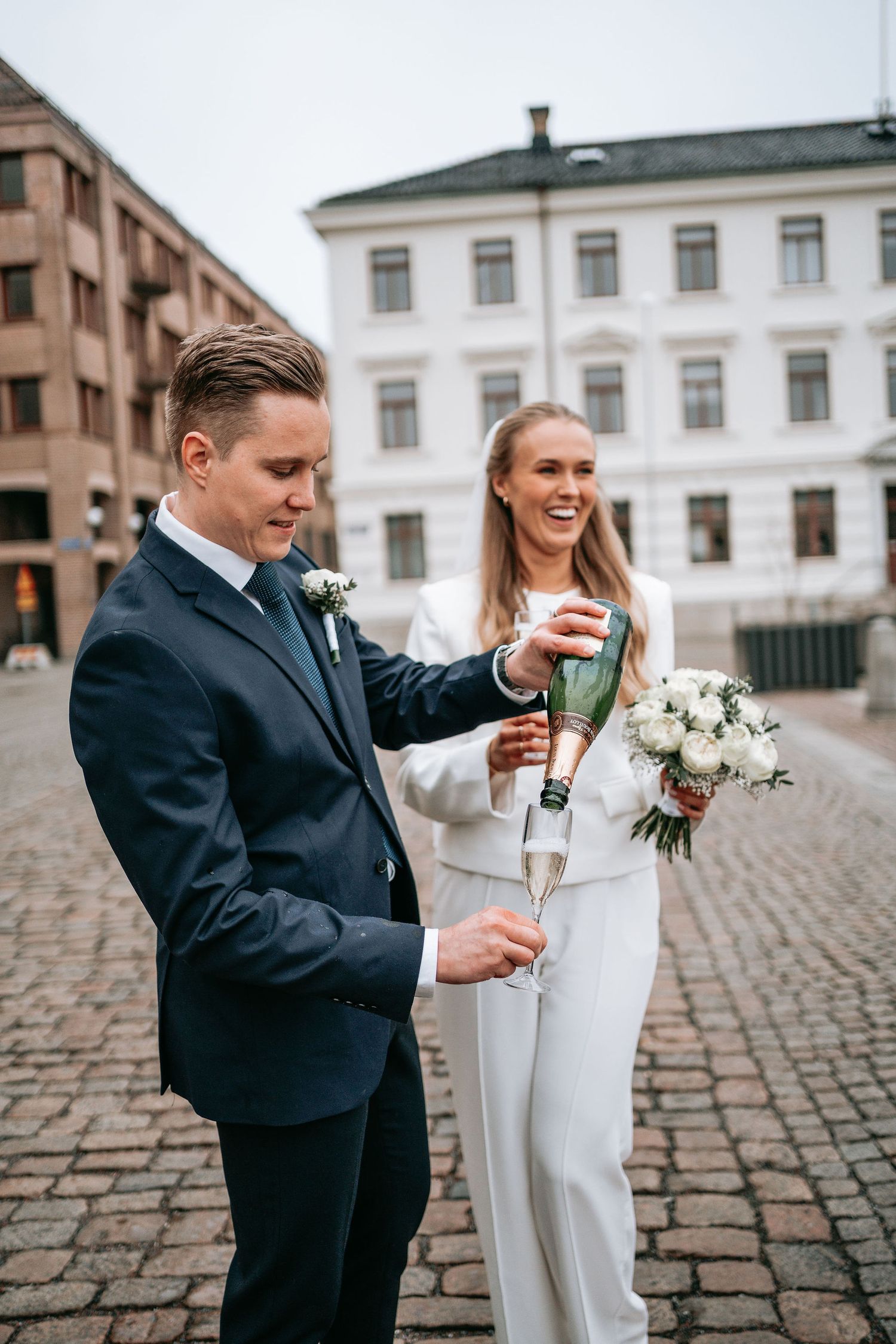 Brudpar firar utanför rådhuset i Göteborg efter vigseln med bubbel. Gifta sig i rådhuset och ha med en fotograf