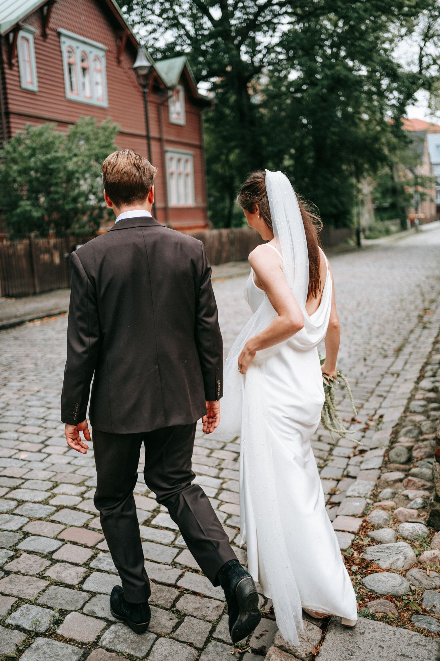 brudpar bakifrån som går på kullerstensgator nära st birgittas kapell i göteborg, bröllopsfotografering, fotograf bröllop, vigsel