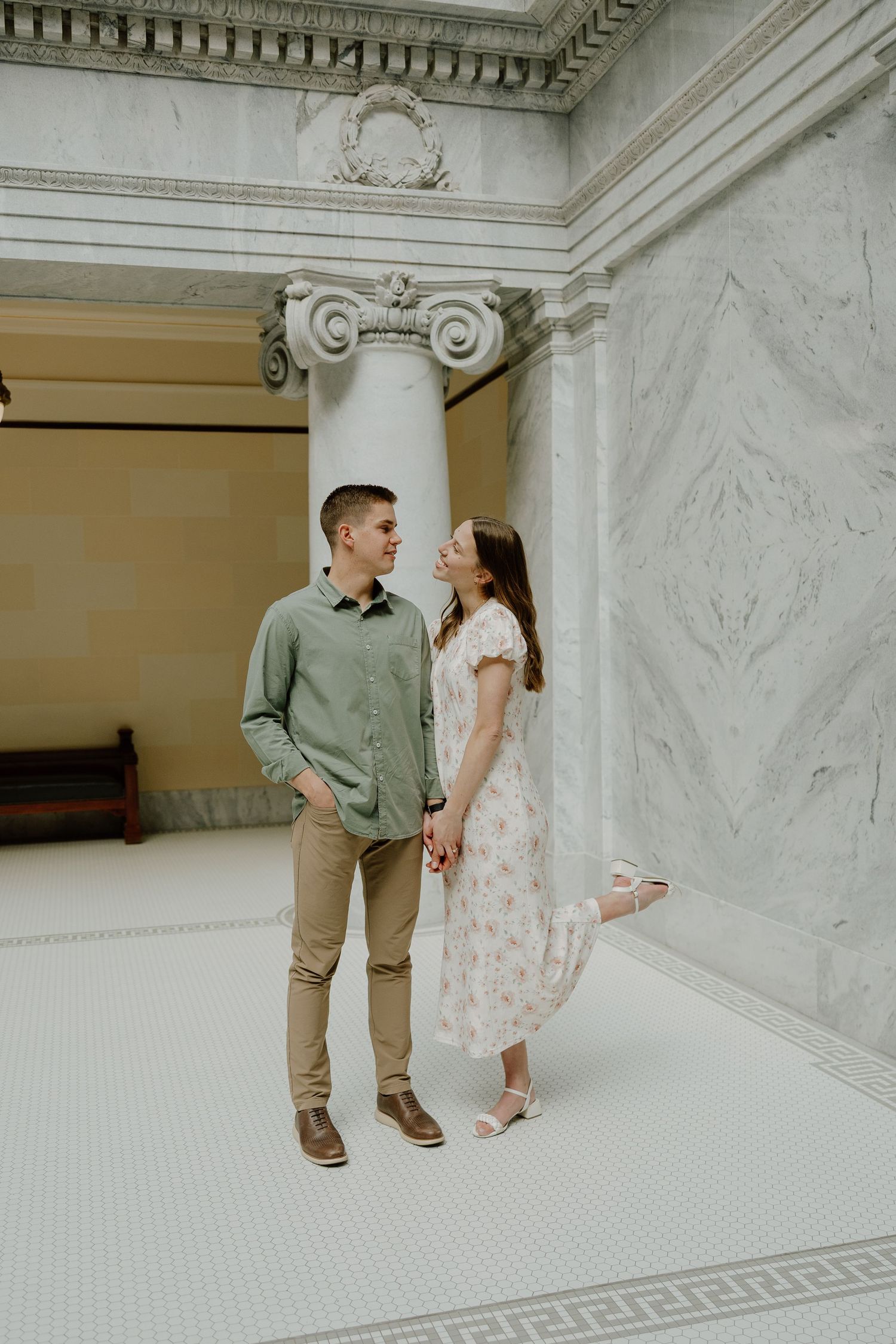 Couple holding hands and gazing at each other in an elegant marble building with ionic columns.