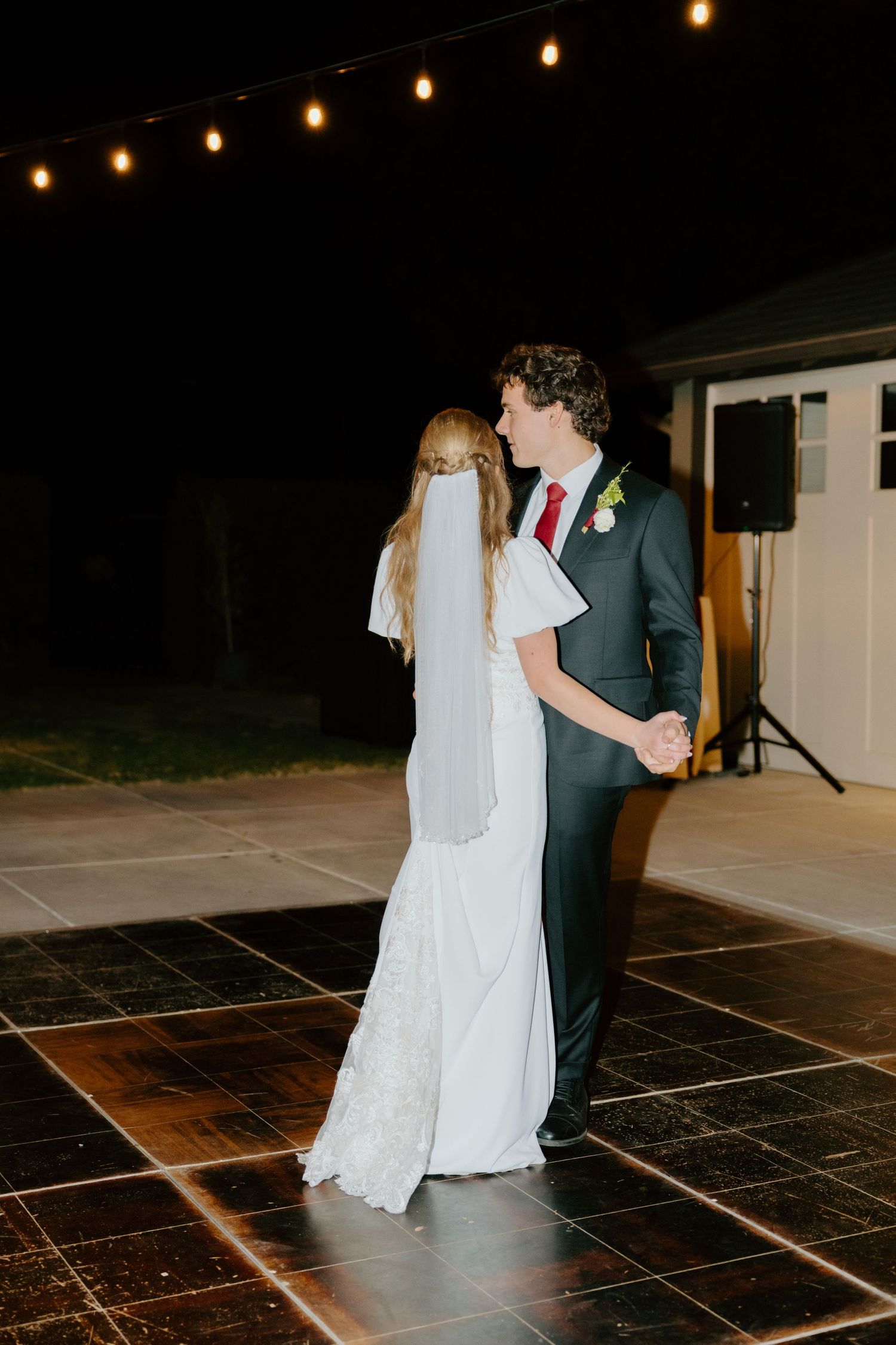 Bride and groom share their first dance under string lights on an outdoor dance floor at night.