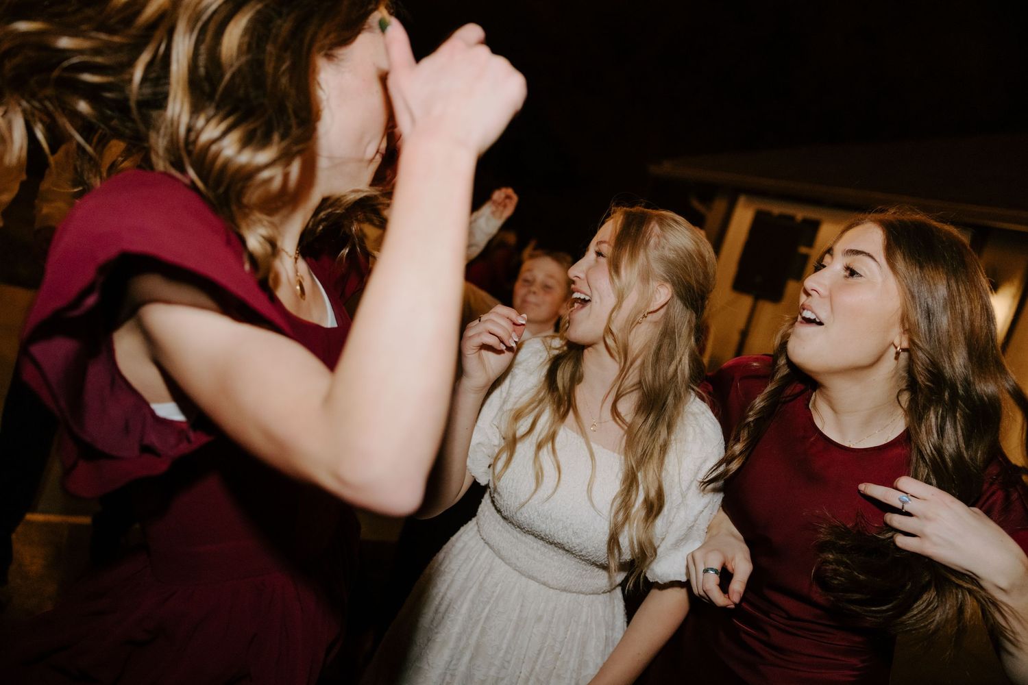 Bridesmaids in burgundy dresses dancing joyfully with bride in white gown at lively wedding reception.