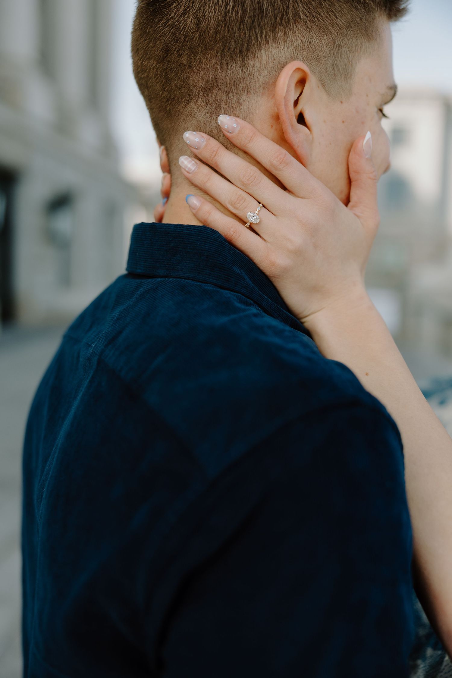 Close-up of a woman's hand with an engagement ring resting on a man's neck during an outdoor photo session.