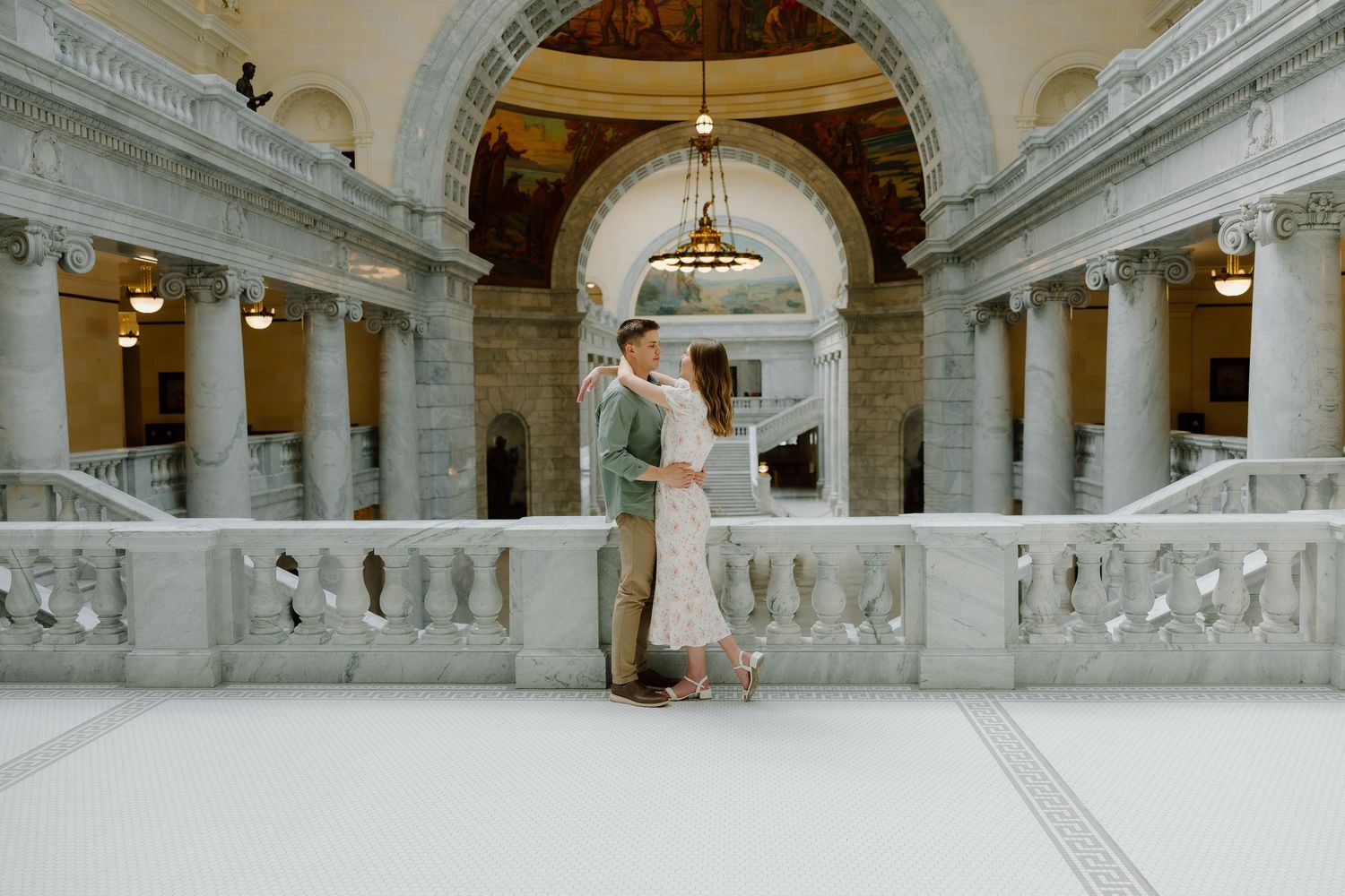 Couple embracing in a grand marble rotunda with tall columns and arched ceilings in a classic government building.