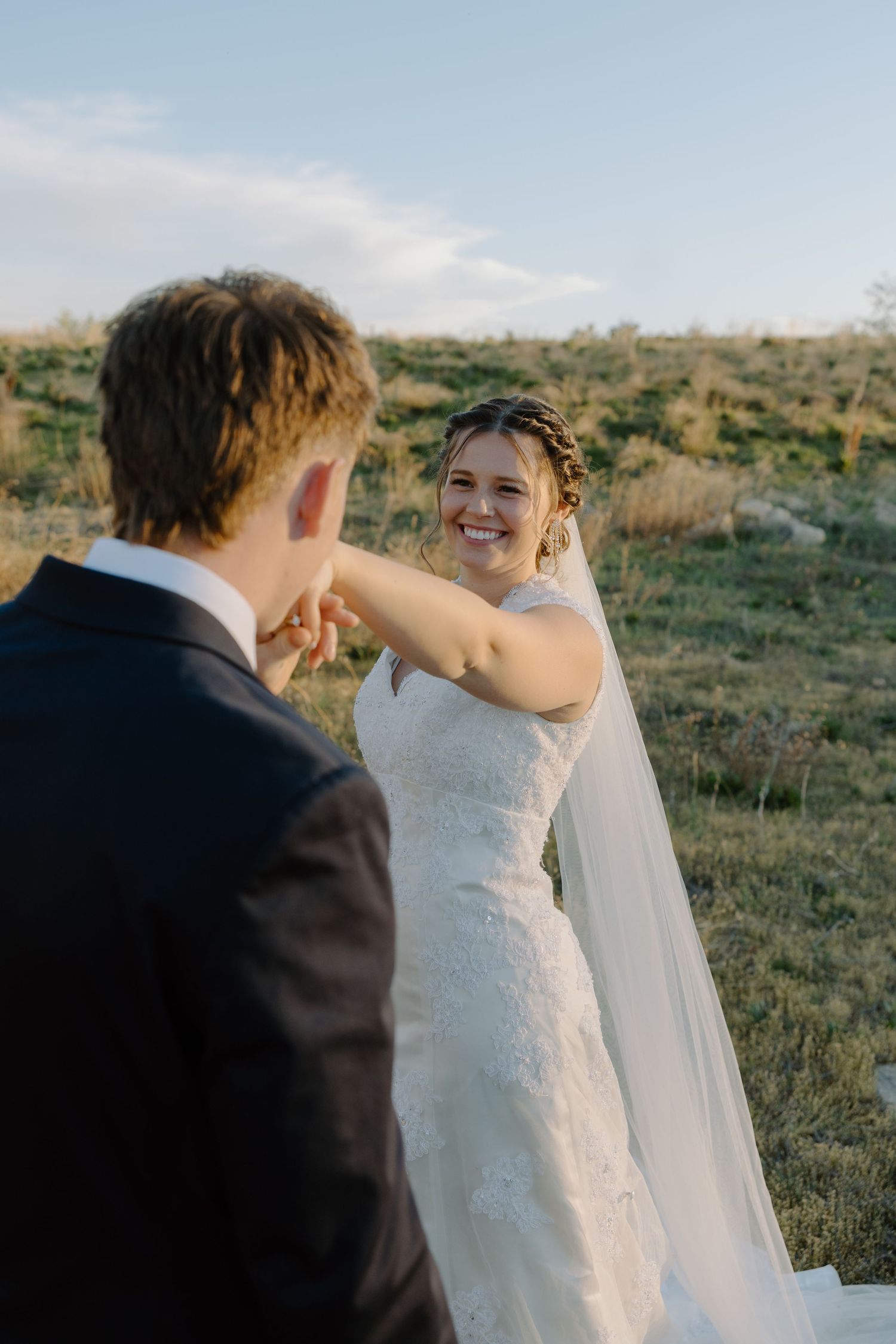 Joyful bride smiles while spinning hand-in-hand with groom in a golden sunlit field.