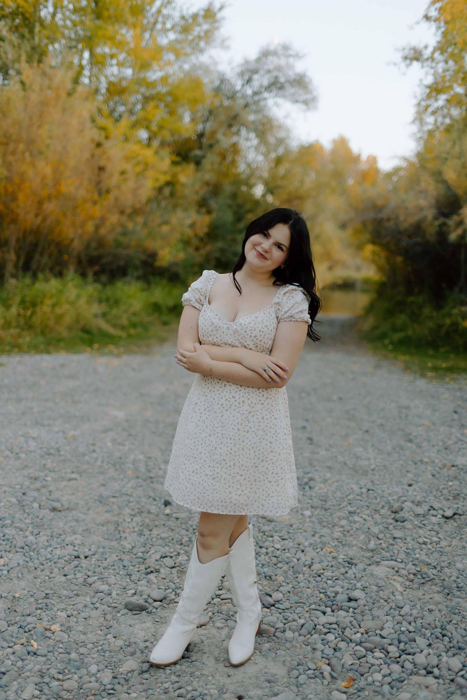 Child in white dress playing on a gravel path surrounded by autumn trees.