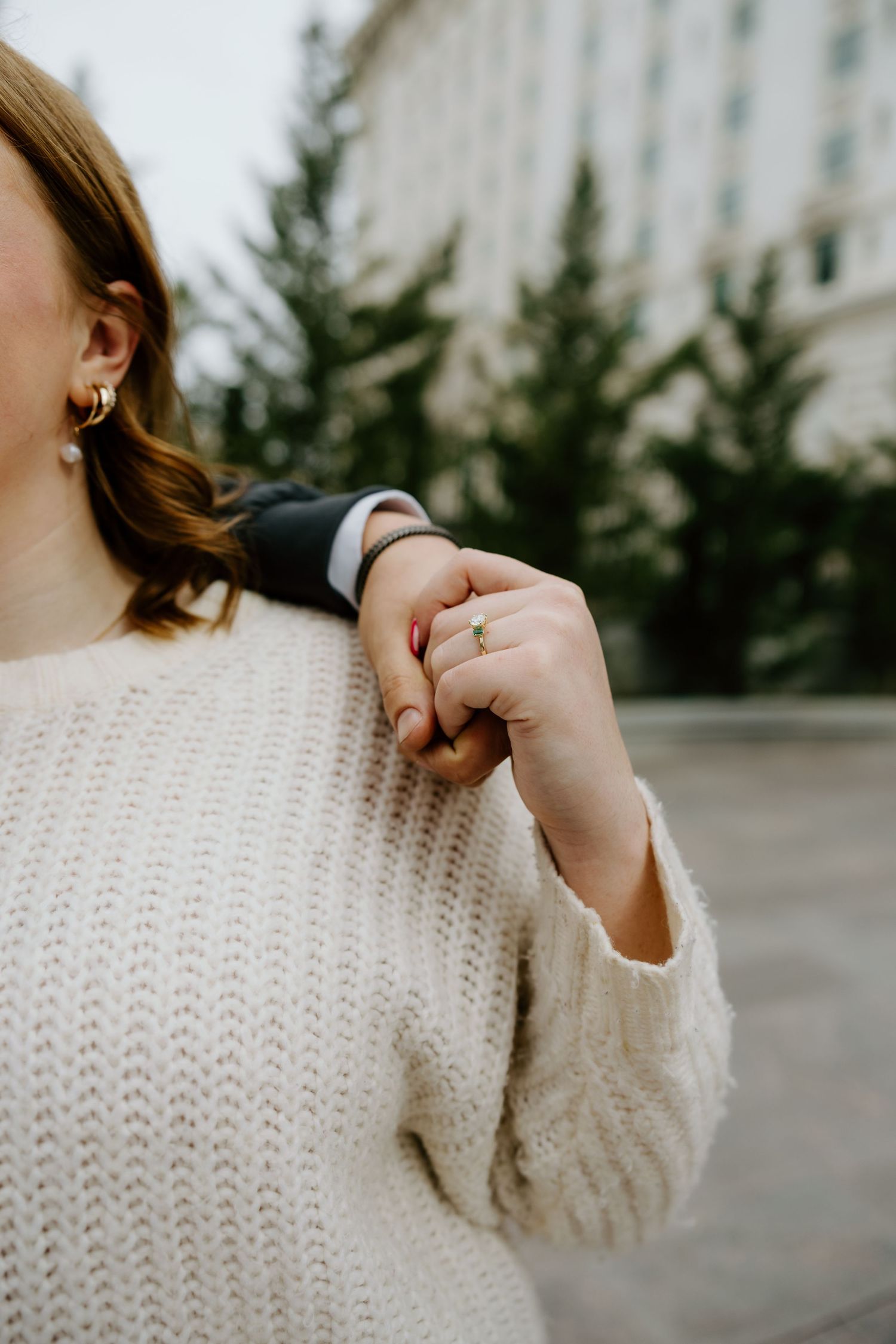 Close-up details of a person wearing a cream knit sweater against an outdoor background.
