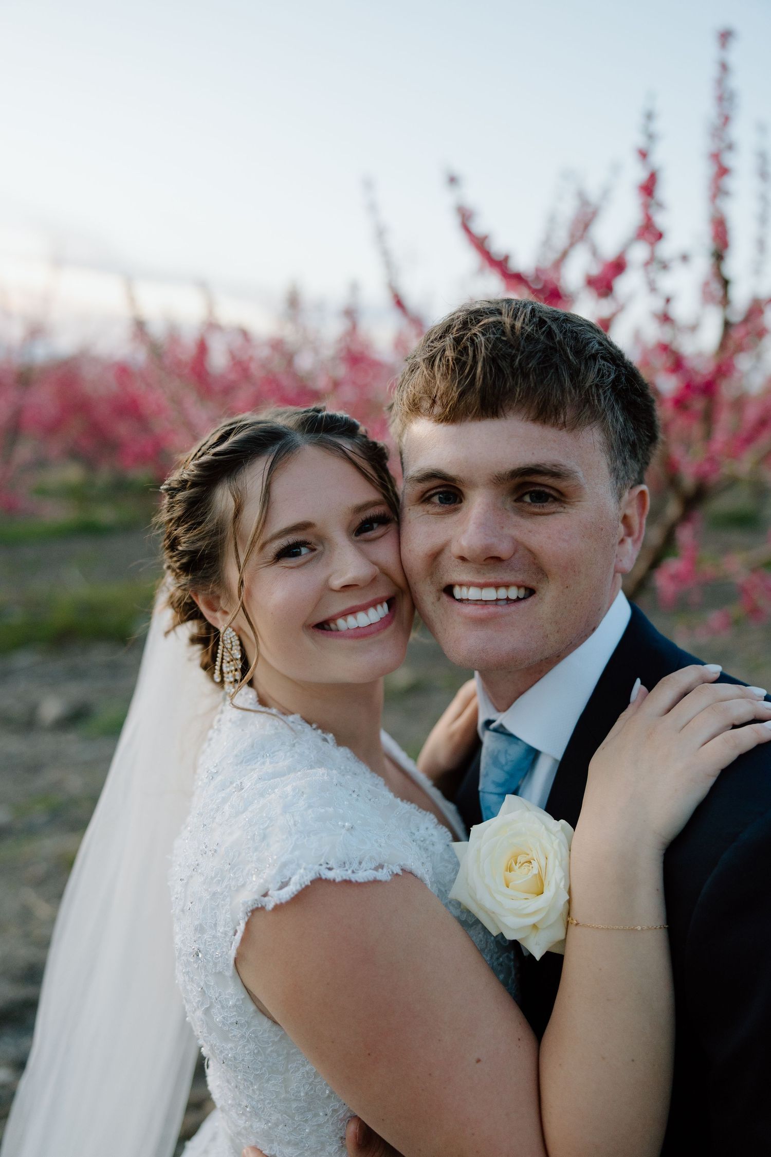 Happy bride and groom posing together in front of pink flowering trees at sunset.