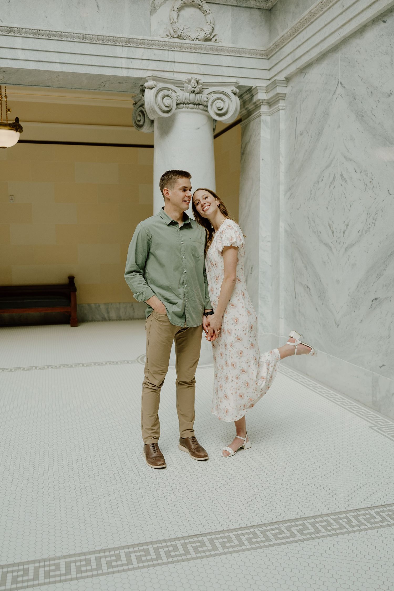 Happy couple holding hands and laughing together in a grand marble hall with ornate columns.