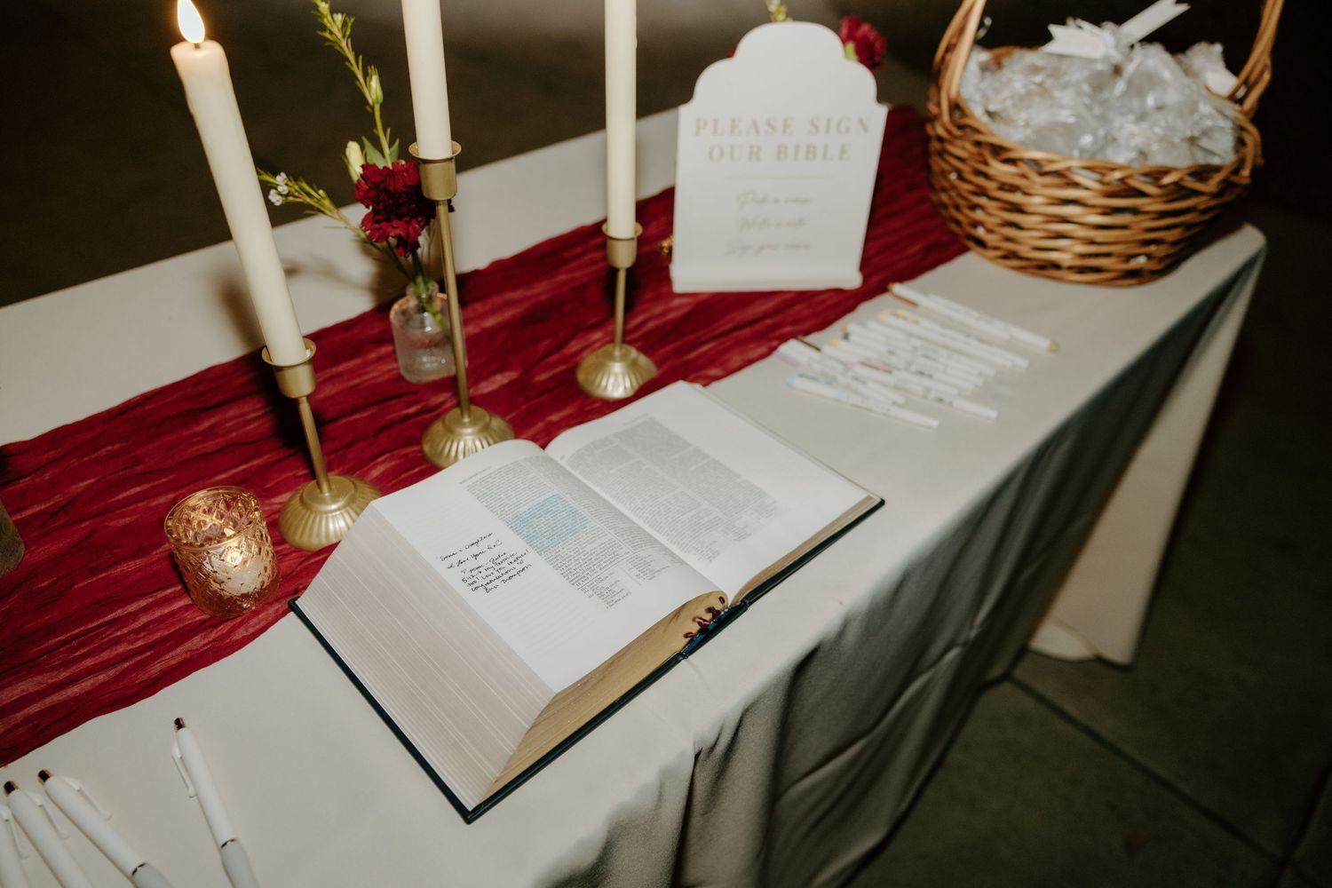 Wedding welcome table with open Bible, candles, burgundy runner, and find your seat sign.