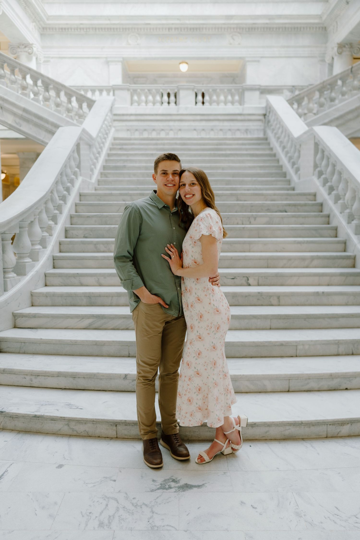 Smiling couple posing together on grand marble staircase in a classical government building.
