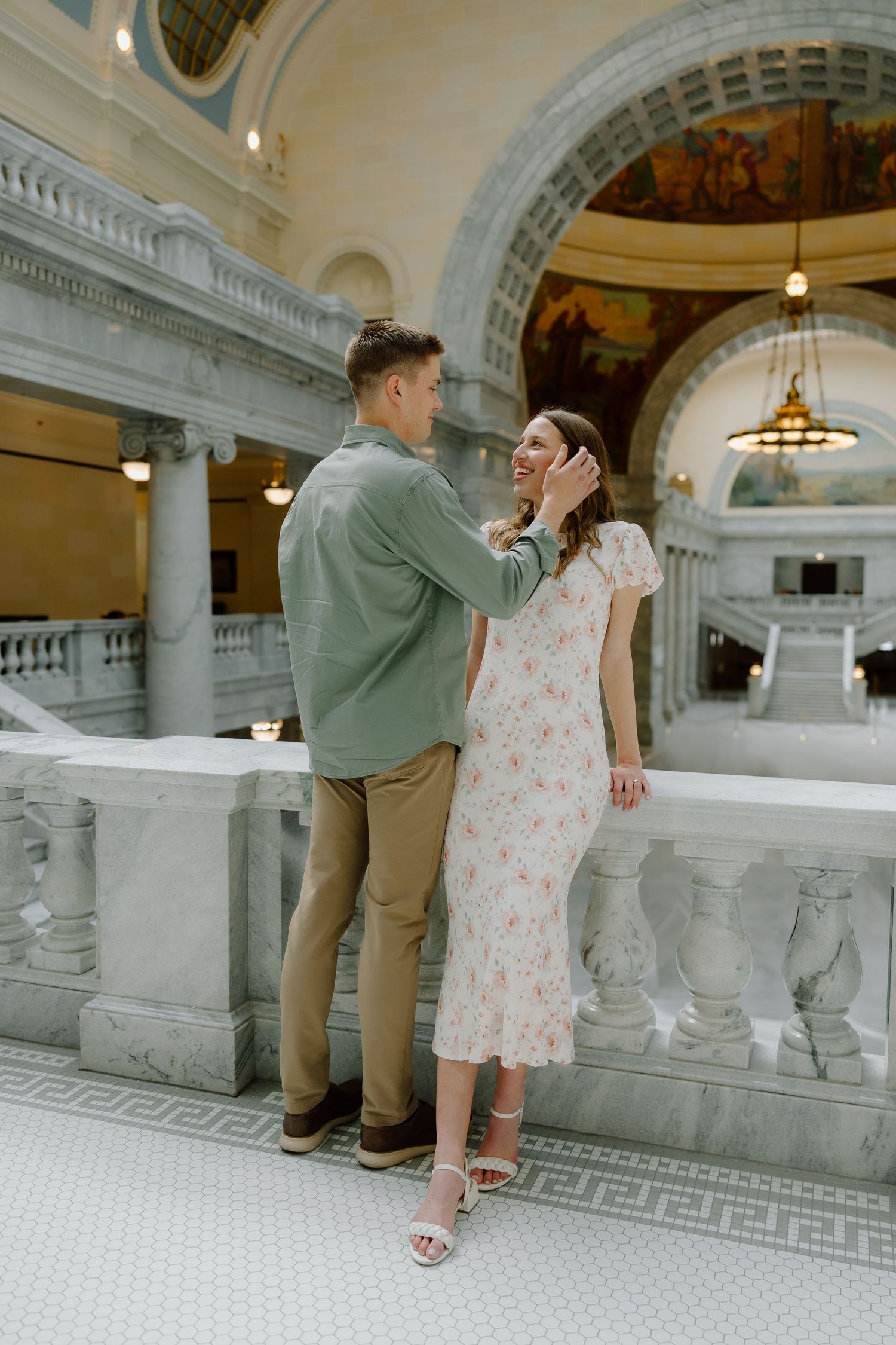 Couple sharing a tender moment in an elegant marble rotunda, man gently touching woman's face.