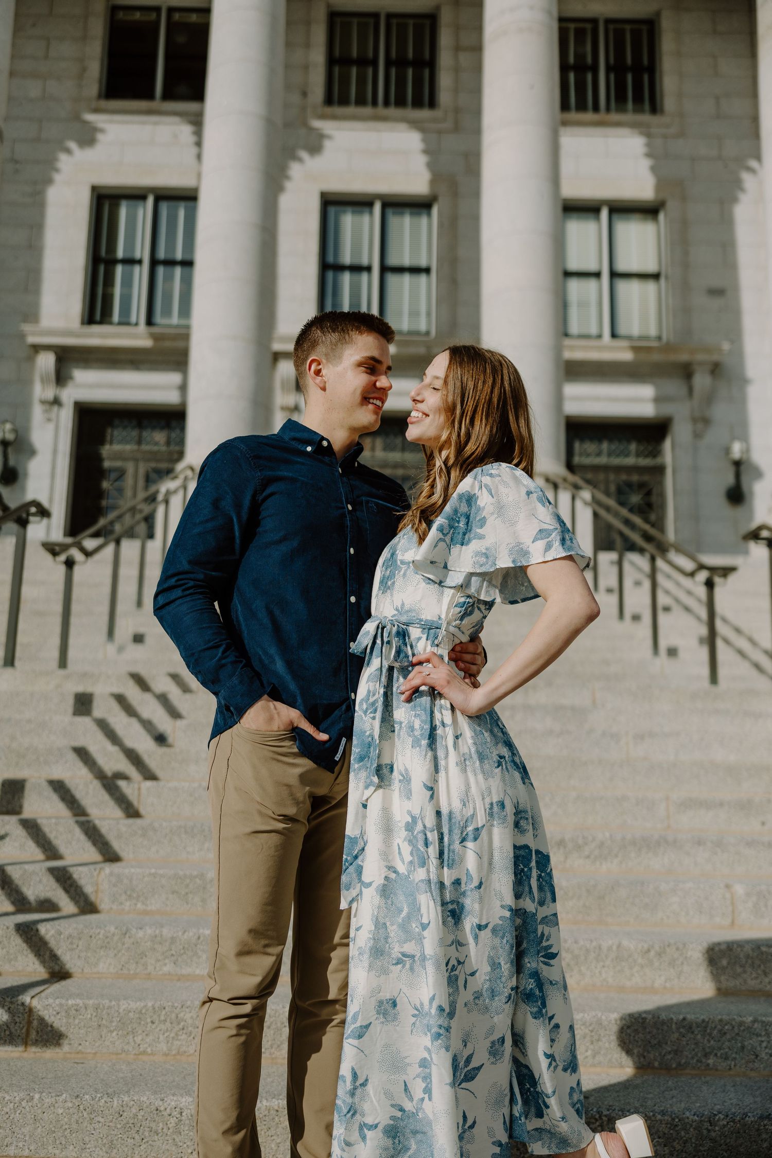 Happy couple gazing at each other on steps of a grand white building during an engagement session.