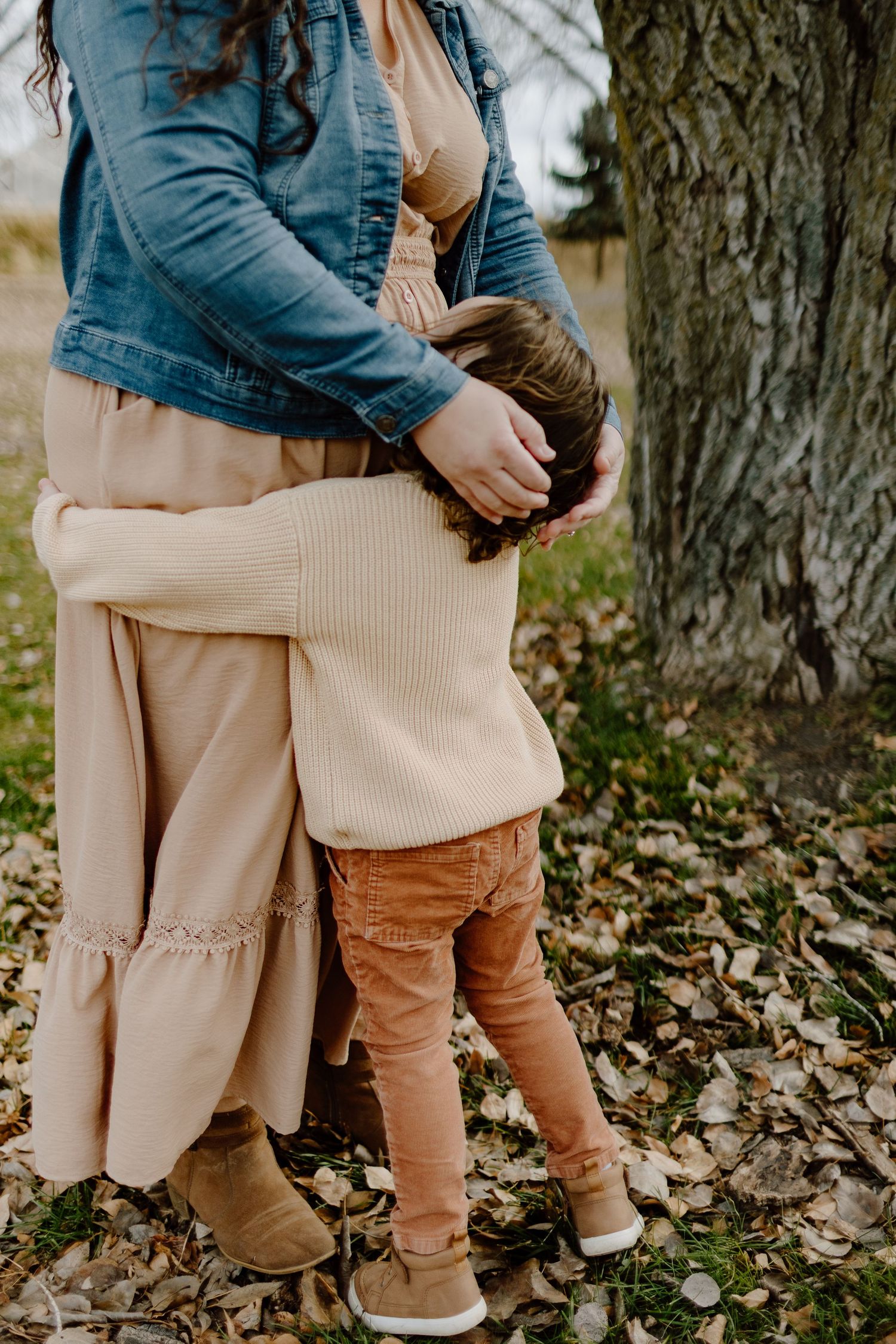 Close-up detail of tan corduroy pants and denim jacket against fallen autumn leaves.