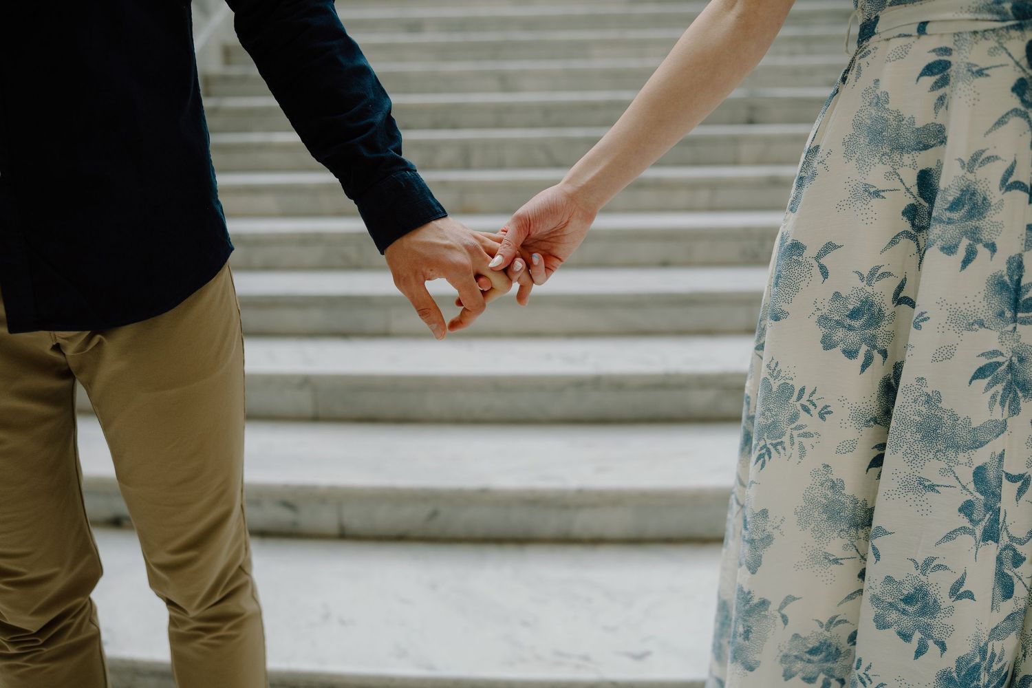 Couple holding hands tenderly in front of stone steps, man in khakis and woman in floral skirt.