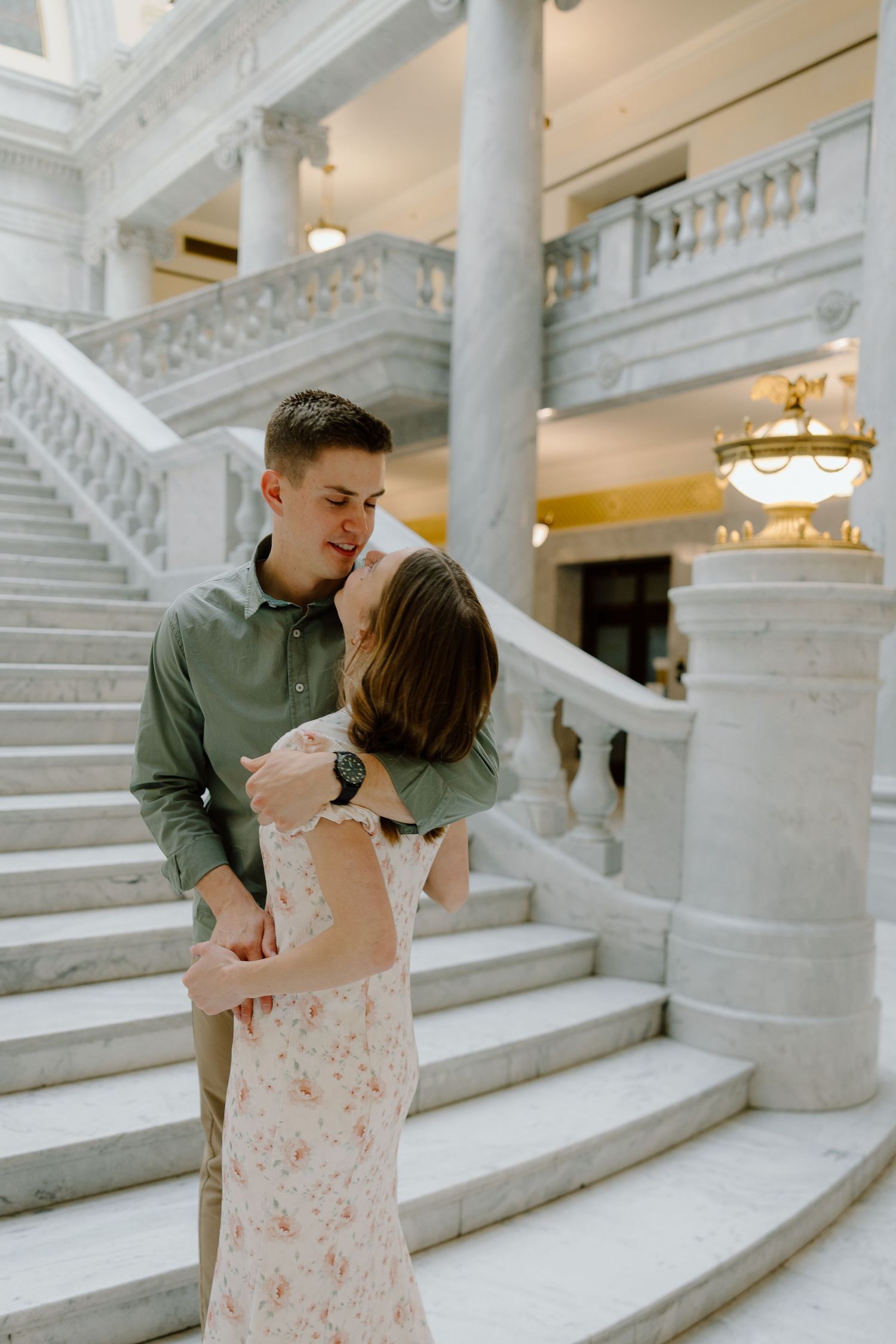 Romantic couple about to kiss in front of a stunning white marble staircase in a classic building.