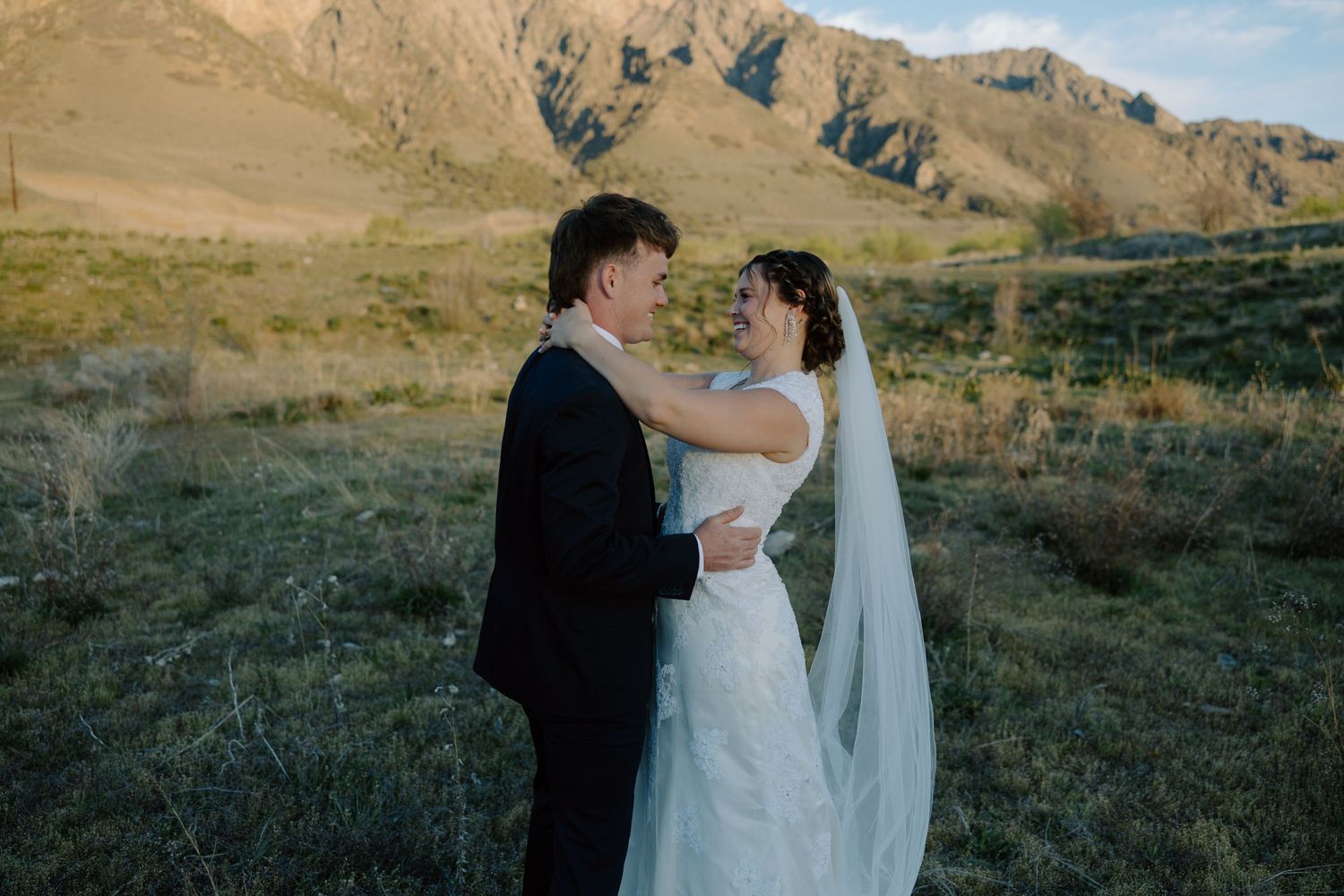 Bride and groom share a romantic moment in a scenic mountain valley, with golden sunlight illuminating the landscape.