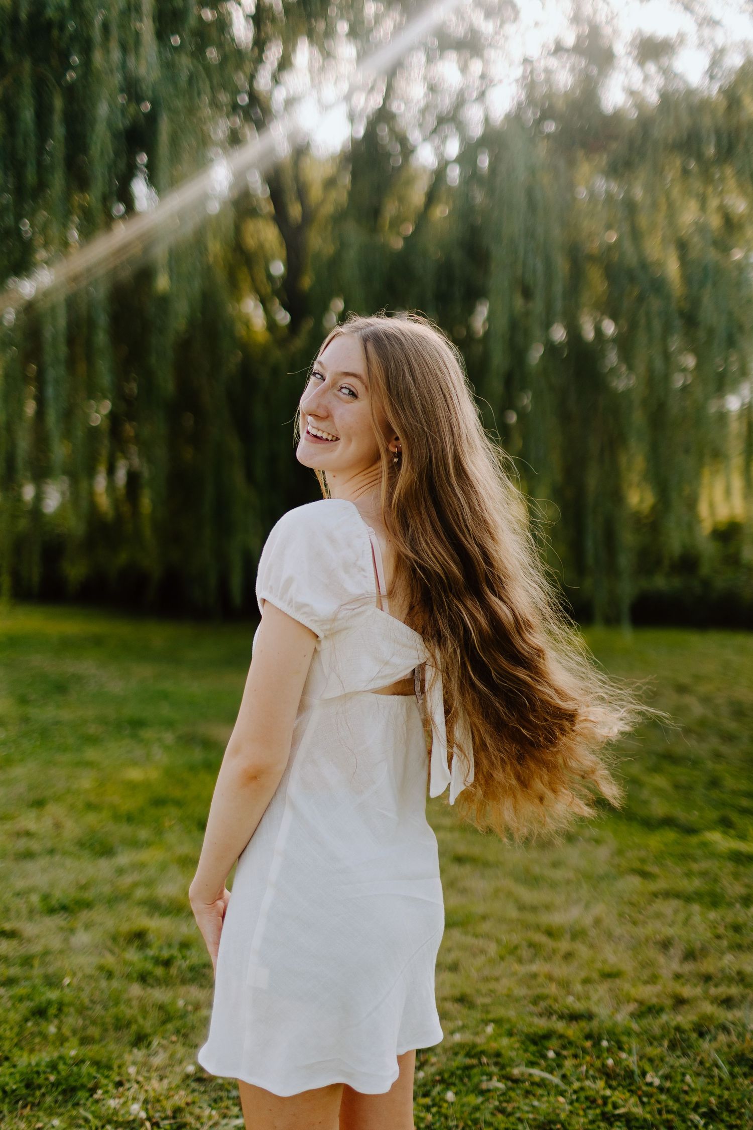 A woman in a white dress twirls joyfully in a sunlit forest setting, creating a carefree summer moment.