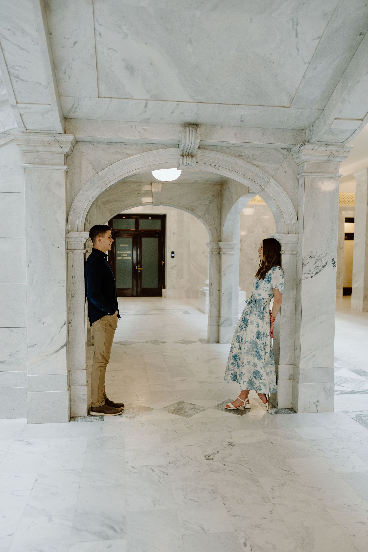 Engaged couple facing each other in a elegant marble archway interior during engagement photos.
