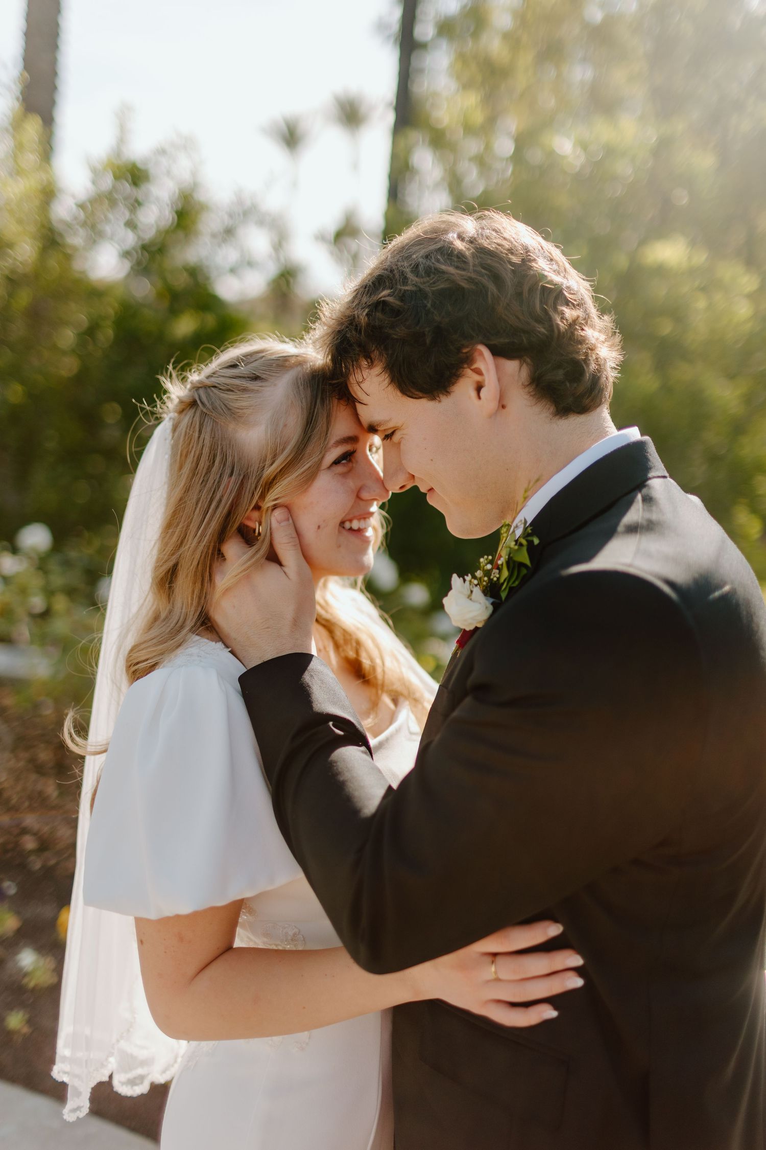 Bride and groom share romantic moment touching foreheads in golden sunlight at outdoor wedding.