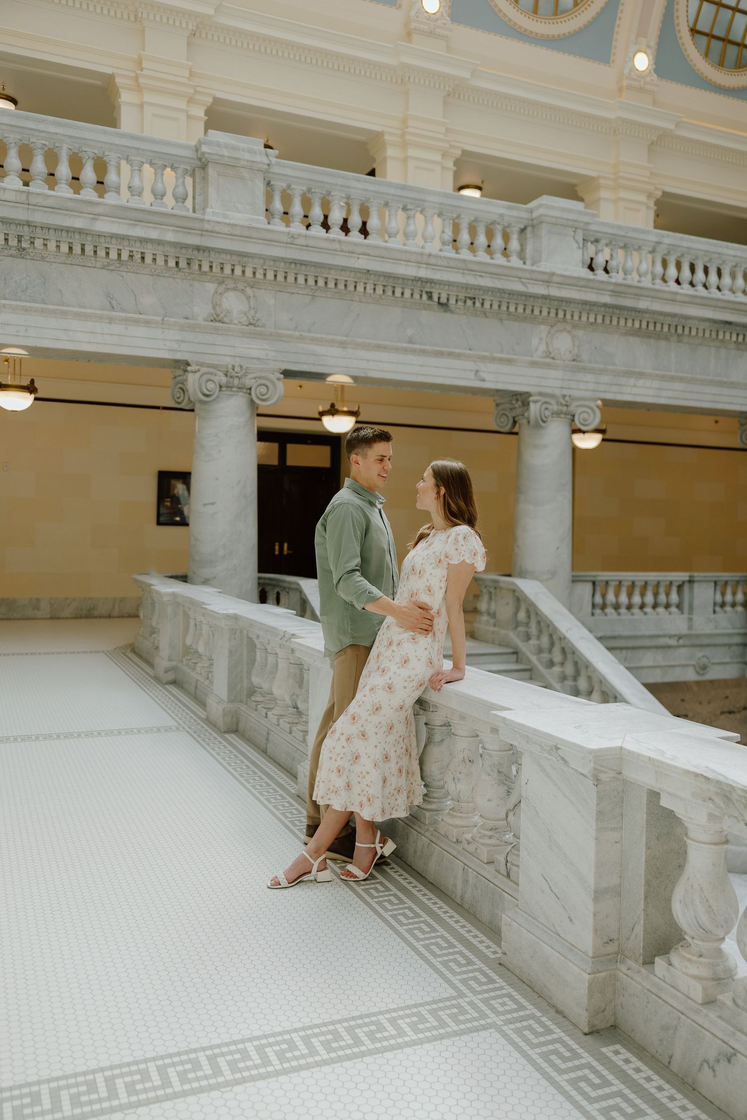 Couple sharing a romantic moment by marble balustrade in an elegant neoclassical building interior.