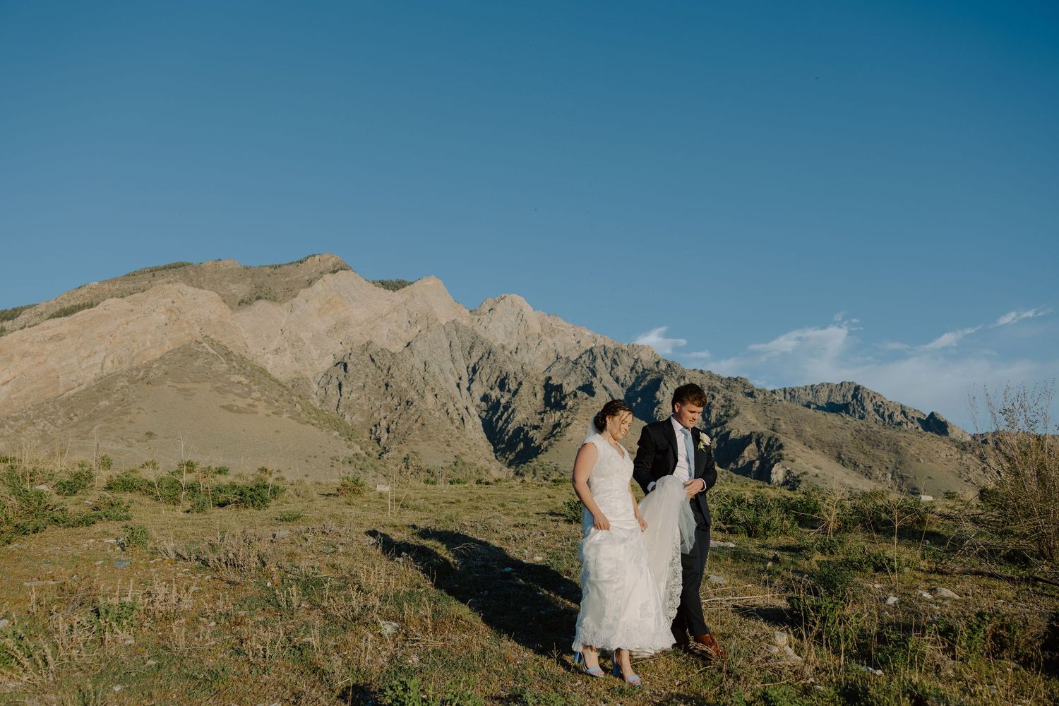 Bride and groom sharing a tender moment on a hillside with rugged mountain backdrop.