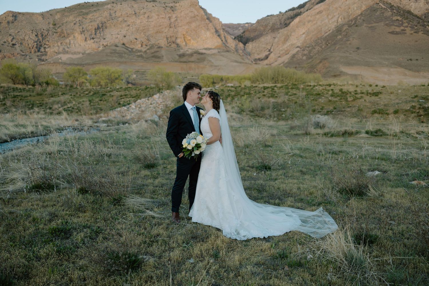 Bride and groom share a romantic moment in a scenic desert landscape with rugged mountains in the background.