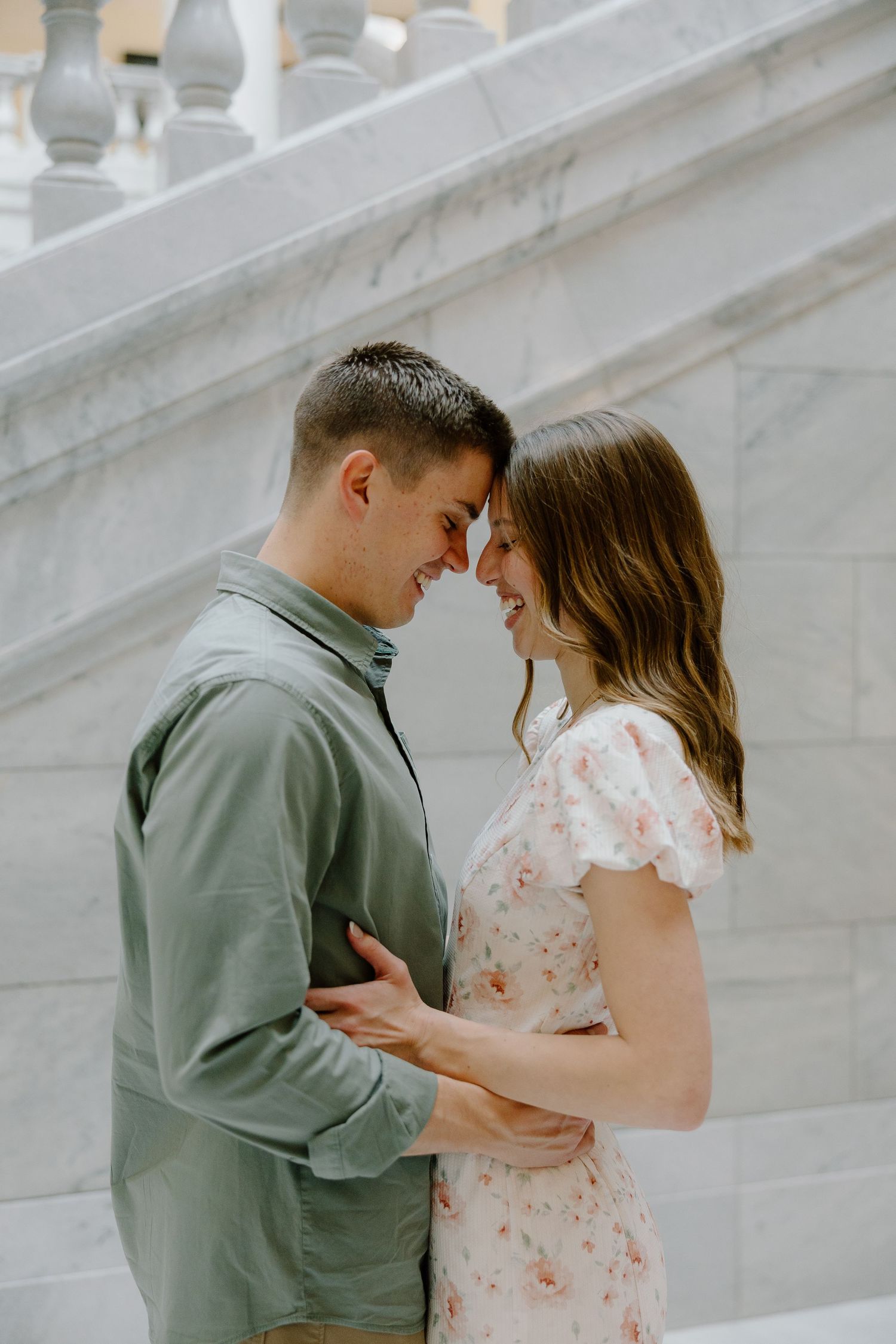 A happy couple touches foreheads and embraces while smiling at each other on marble steps outdoors.
