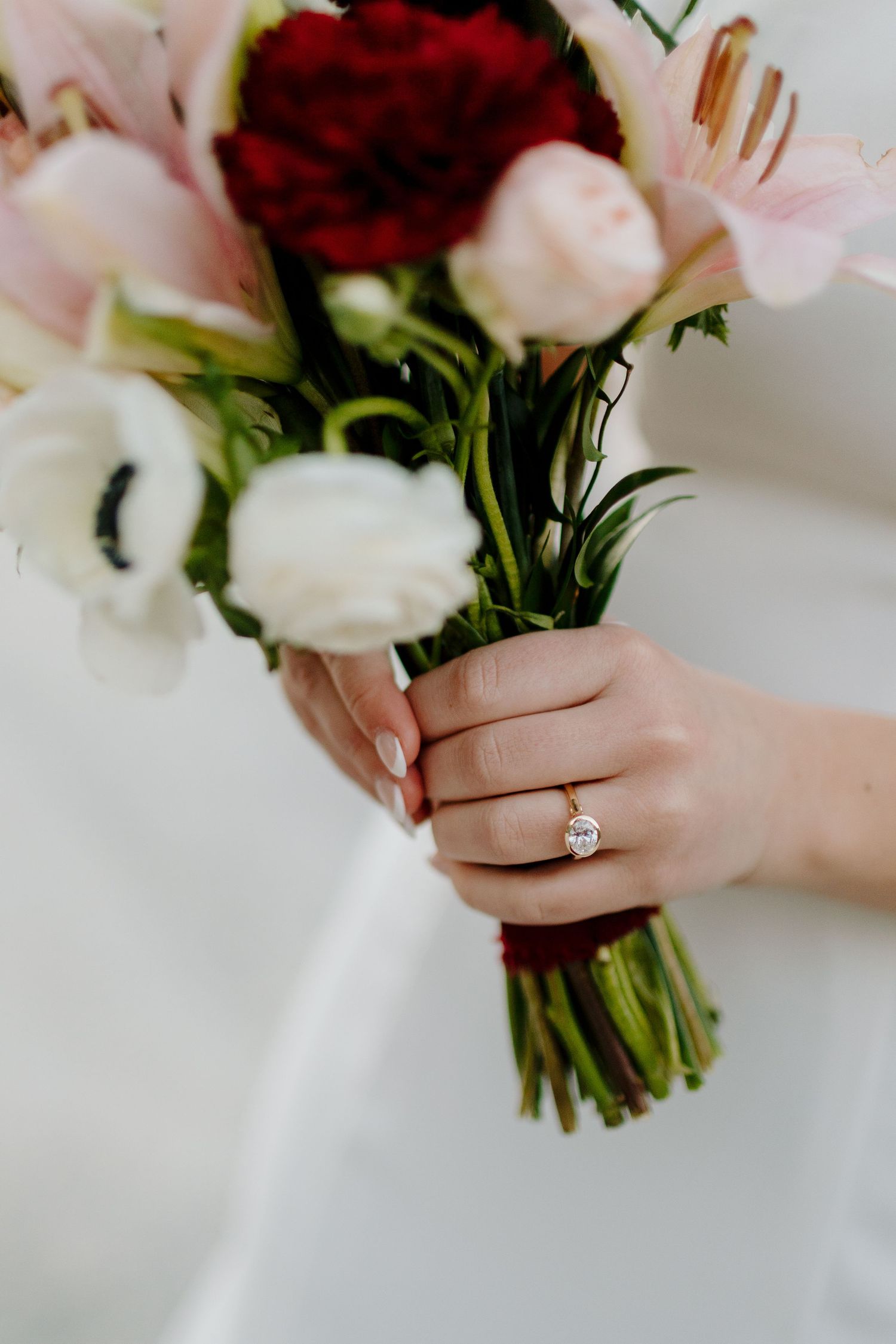 Close-up of bride's hand holding colorful wedding bouquet with pink lilies, red roses, and white anemones.
