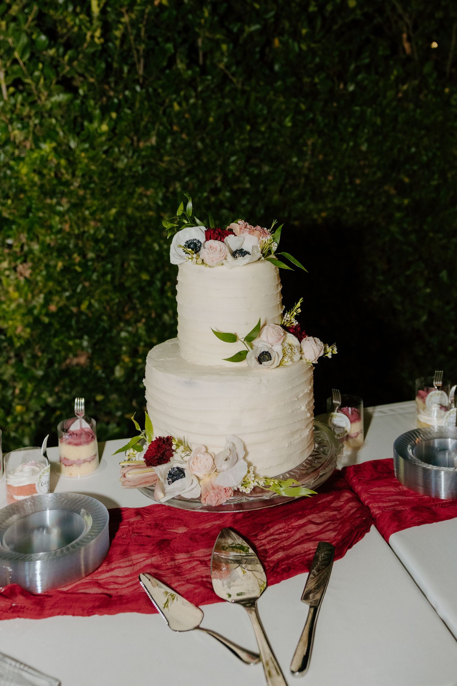 Three-tier white textured wedding cake decorated with anemone and pink flowers on burgundy table runner.