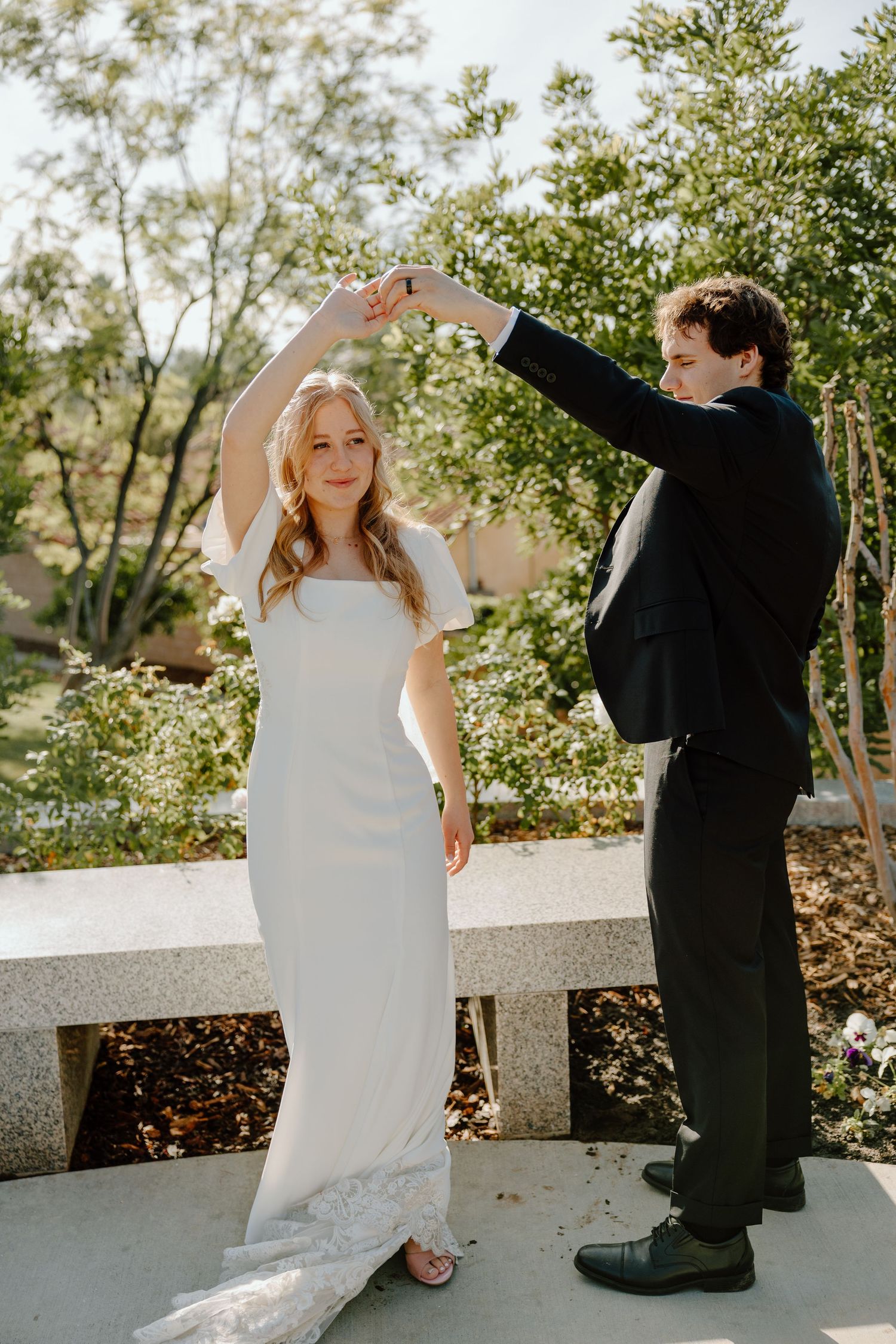 Bride and groom dancing outdoors, groom spinning bride in white wedding dress.