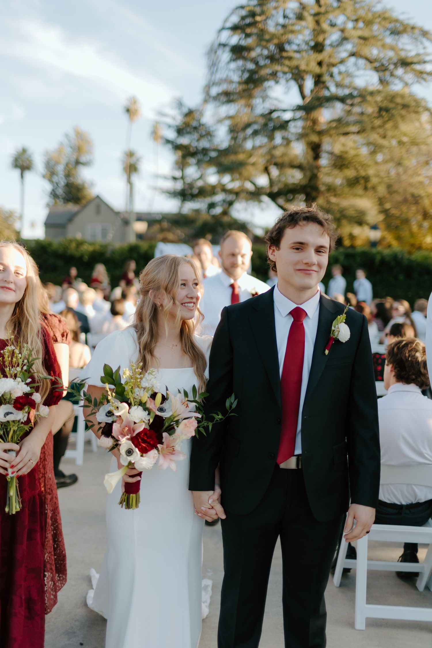Bride and groom walk down the aisle hand in hand at an outdoor wedding ceremony with guests seated nearby.